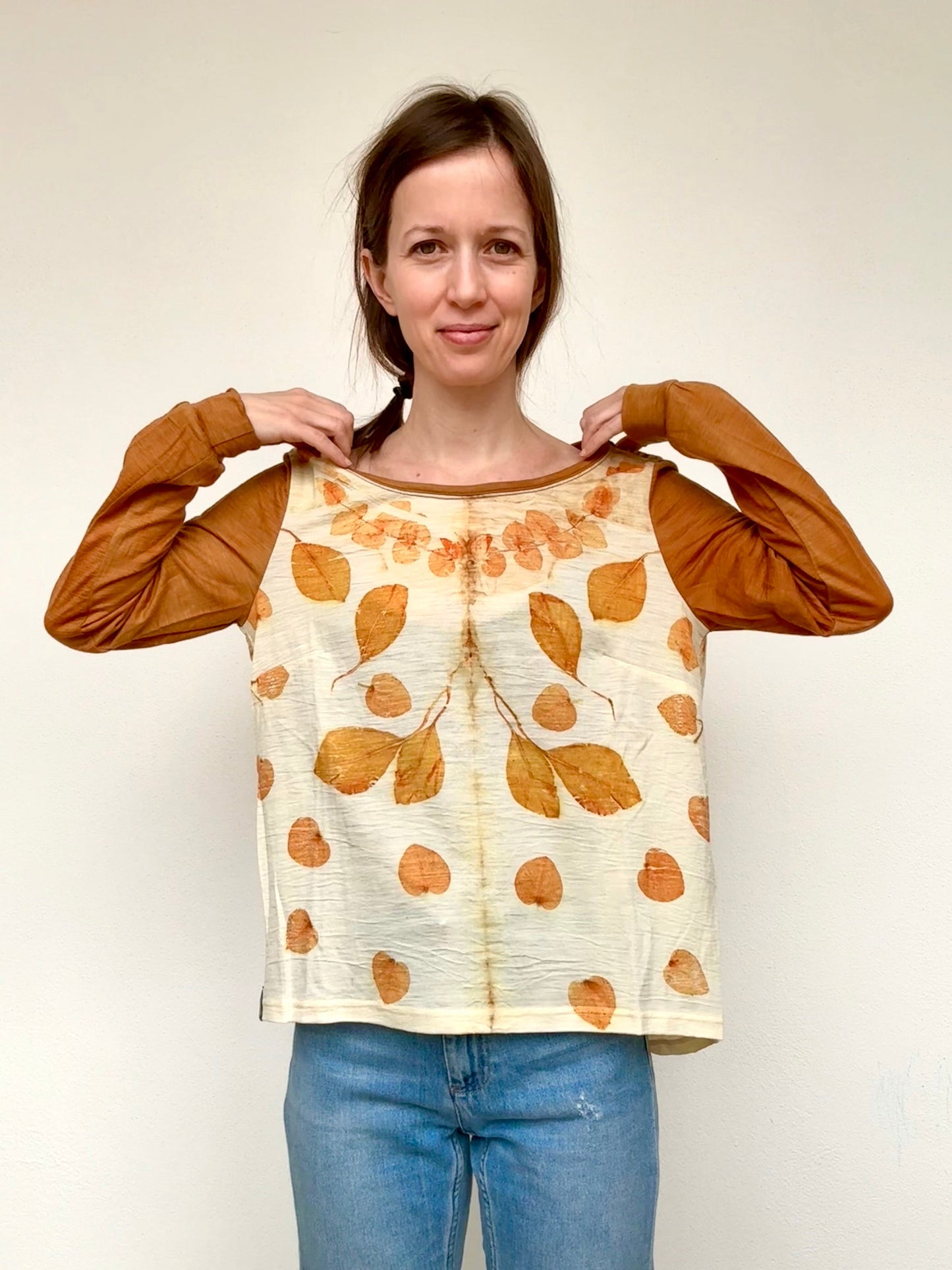 Woman wearing a beige, orange dyed long-sleeve top with orange eucalyptus leaf pattern and blue jeans against a plain background by DOT 'N' POT