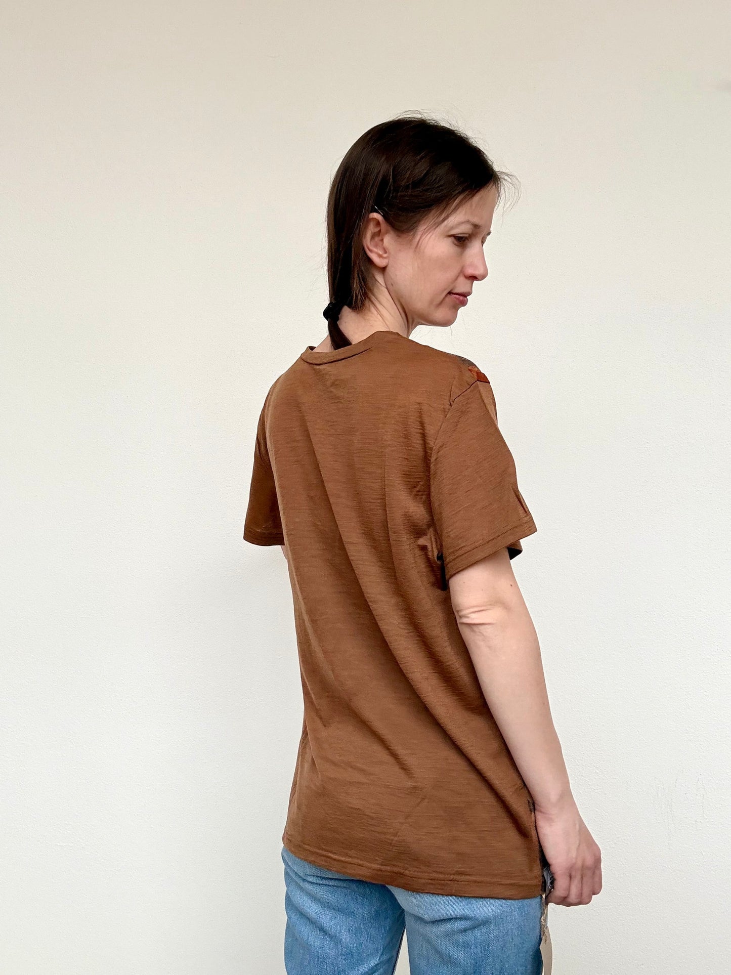 Woman wearing a naturally brown dyed t-shirt and blue jeans against a white background