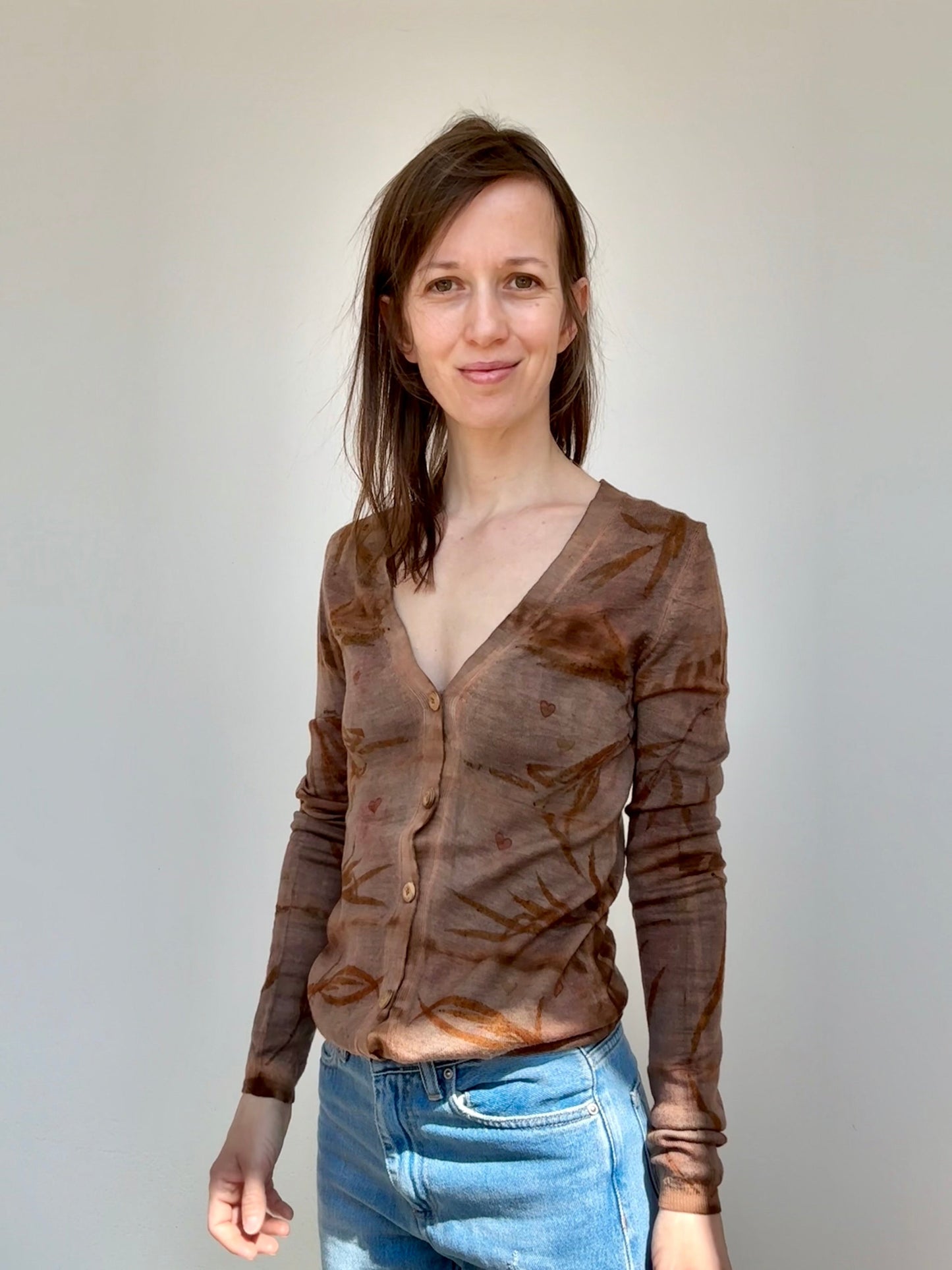 Woman wearing a brown shibori sweater and blue jeans against a plain background