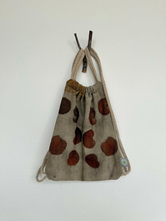 Drawstring bag with brown, orange, red heart shaped eucalyptus leaves pattern on a white background by DOT 'N' POT