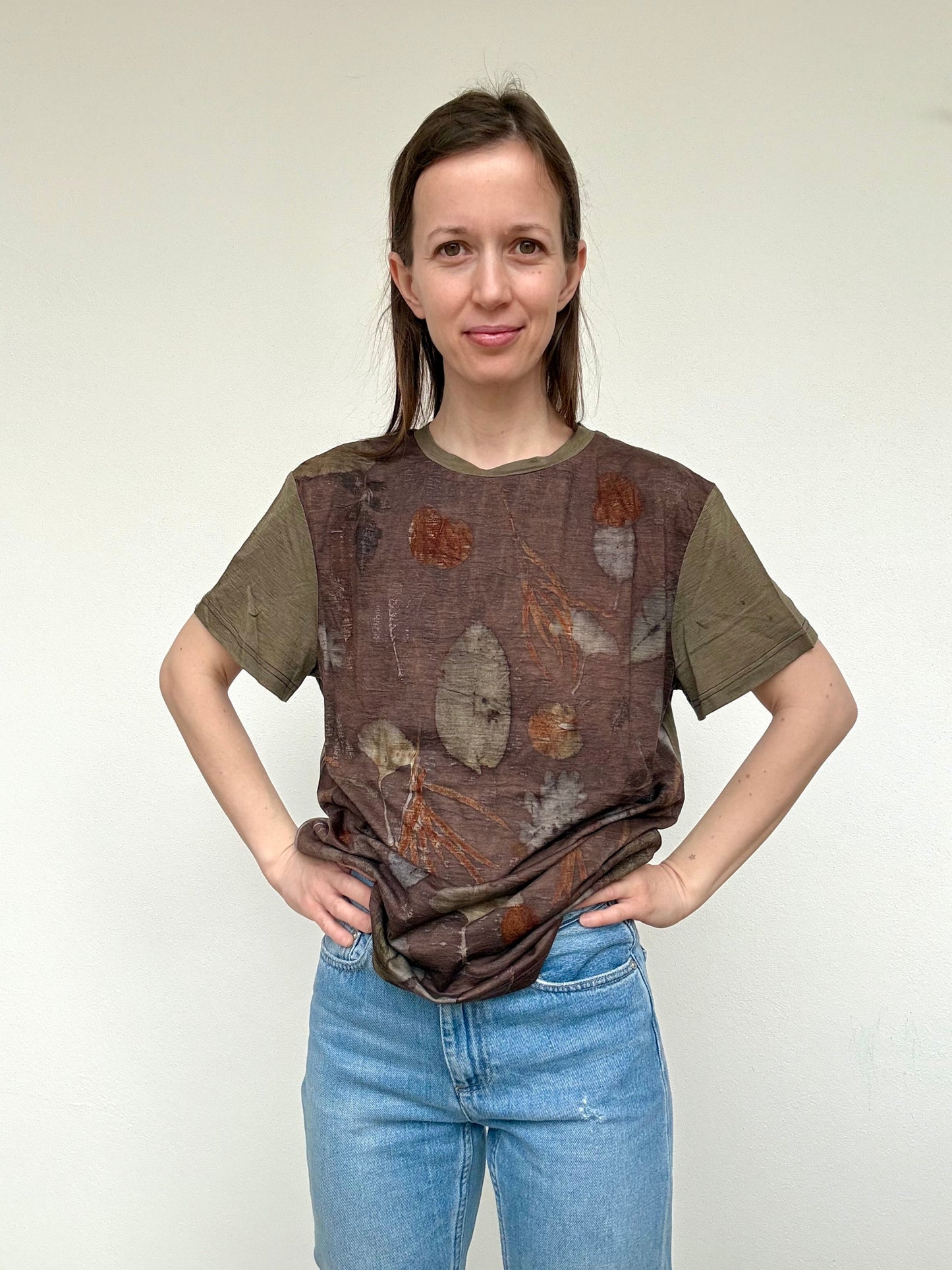 Person wearing a colorful sweet chestnut dyed merino t-shirt with leaf patterns and blue jeans against a white background by DOT 'N' POT