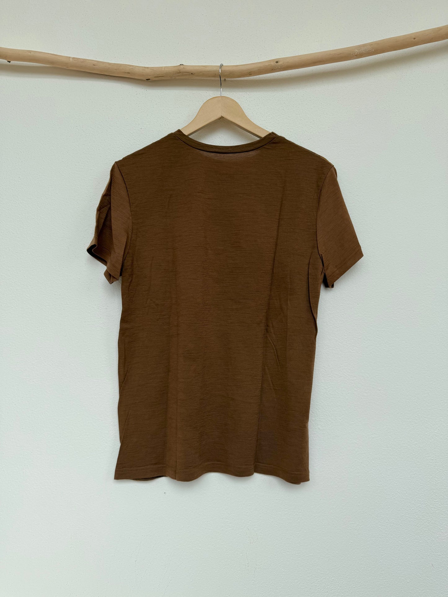 back part of a brown naturally dyed t-shirt dyed with walnut husks, on a hanger against a white wall