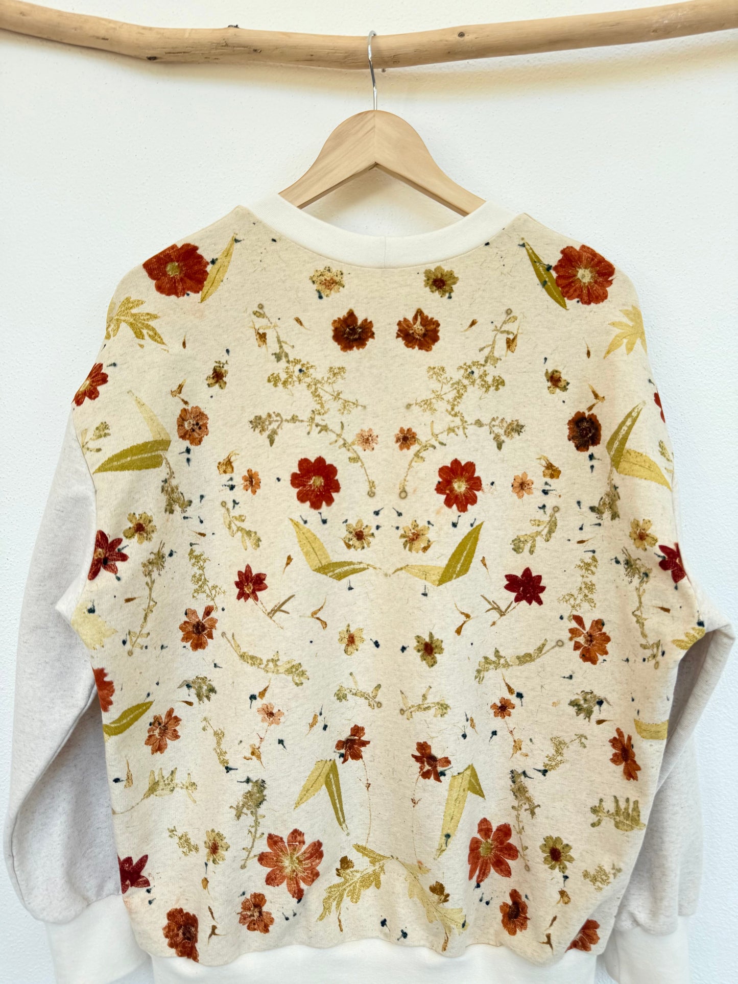 Floral-patterned sweater on a hanger against a white wall - eco-printed with plants