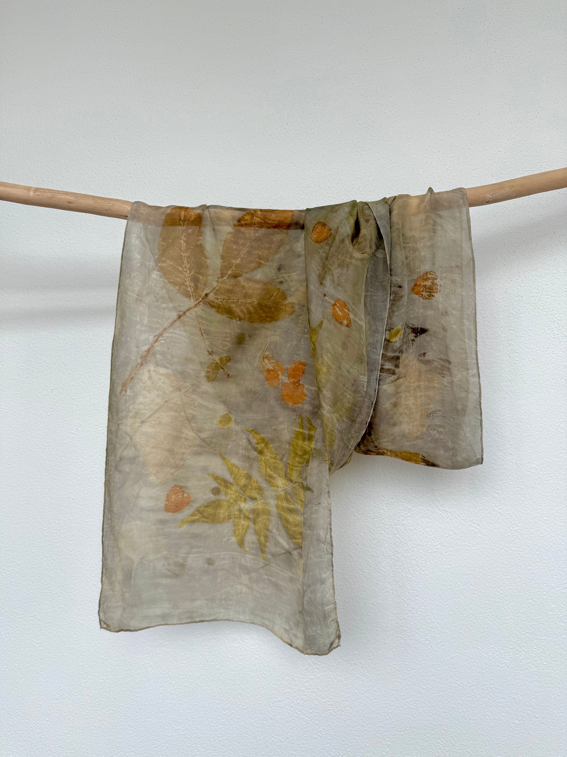 eco-printed silk scarf with various leaves like eucalyptus, rhus typhina and walnut hanging from a wooden rod by DOT 'N' POT