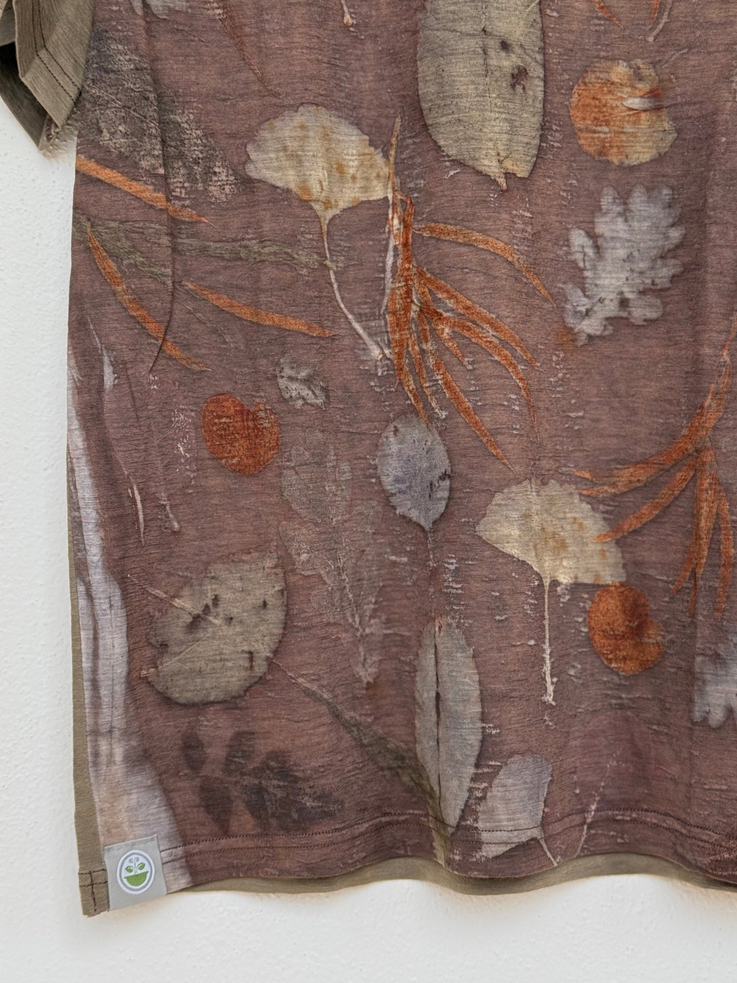 detail of the front part of an eco-printed plant patterned t-shirt with logo by DOT 'N' POT