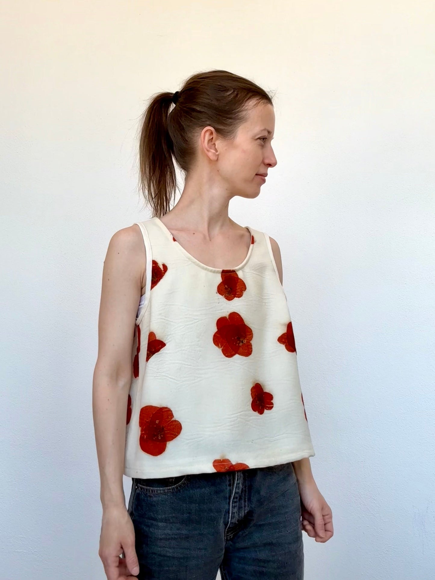 Woman wearing a sleeveless merino wool top with red floral patterns against a plain background - eco-printed with eucalyptus leaves by DOT 'N' POT