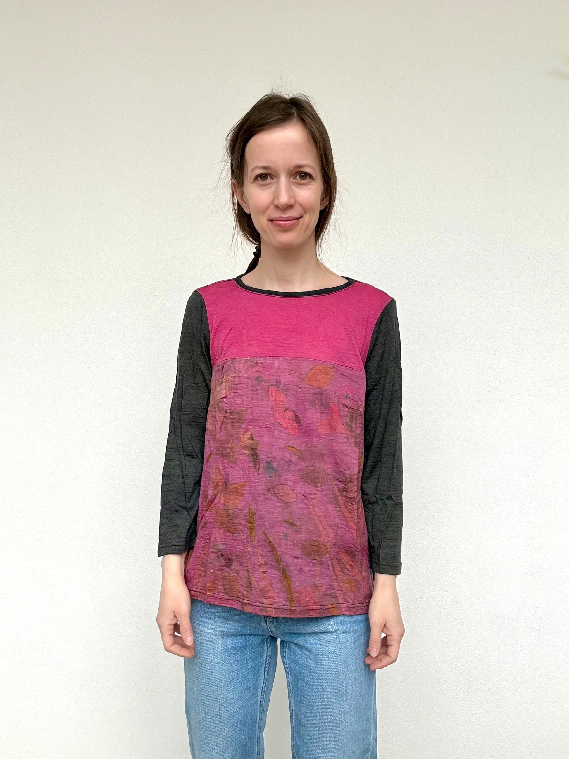 Woman wearing a pink and gray eco-printed, patterned top with blue jeans against a white background