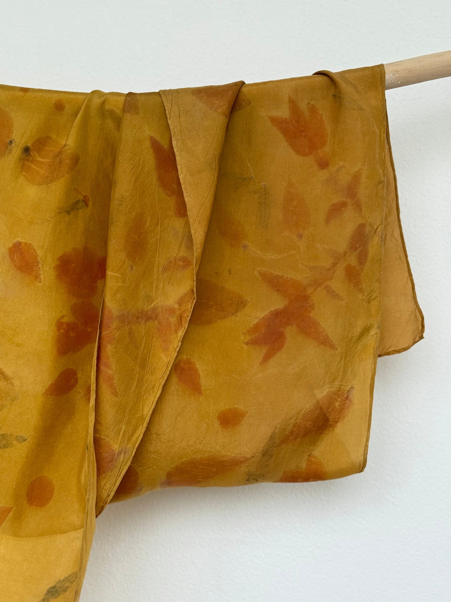 silk scarf naturally dyed with onion skins and eco-printed with eucalyptus leaves on a wooden rod