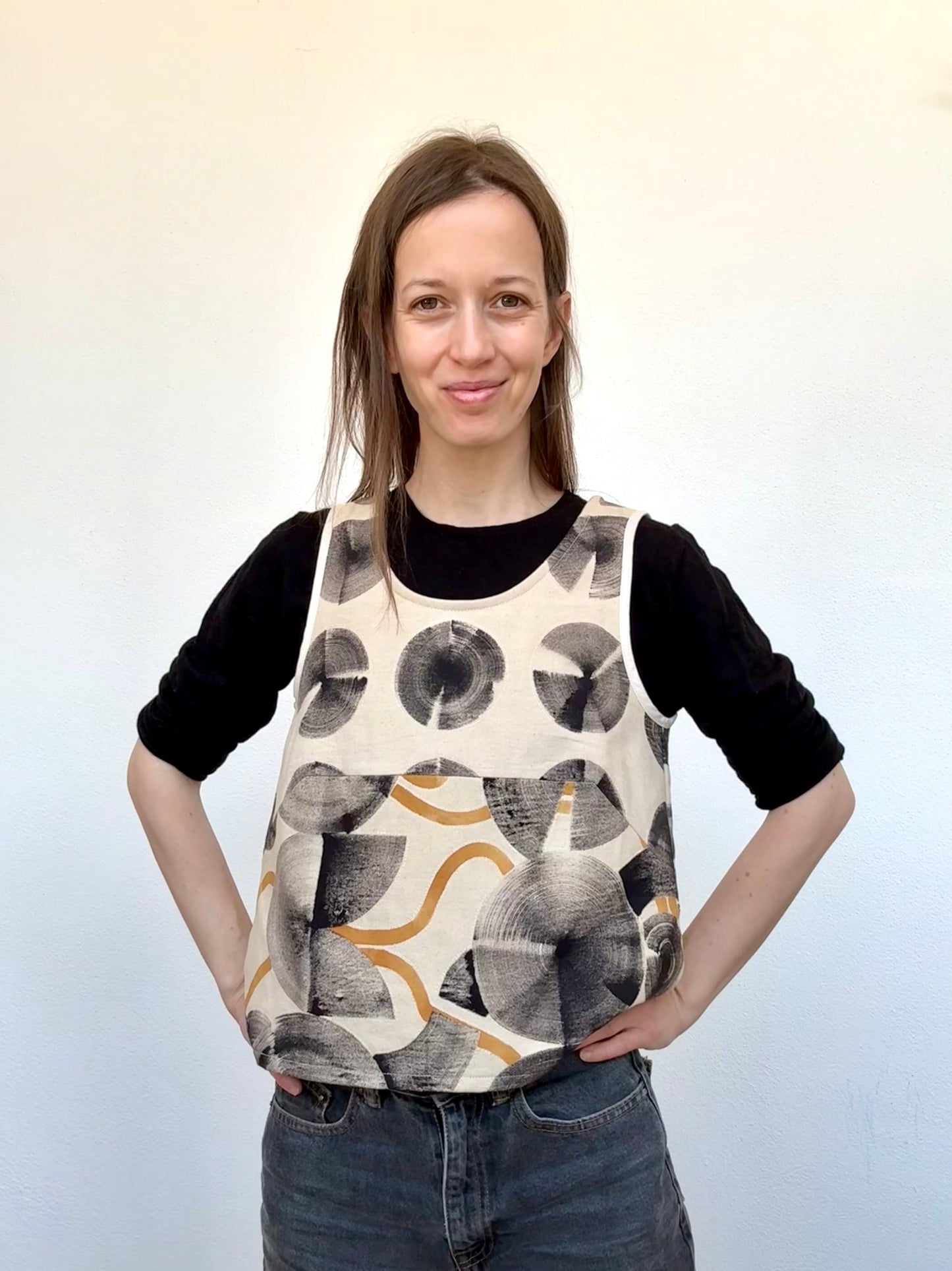 Woman wearing a patterned and hand-painted top over a black long-sleeve shirt against a white background