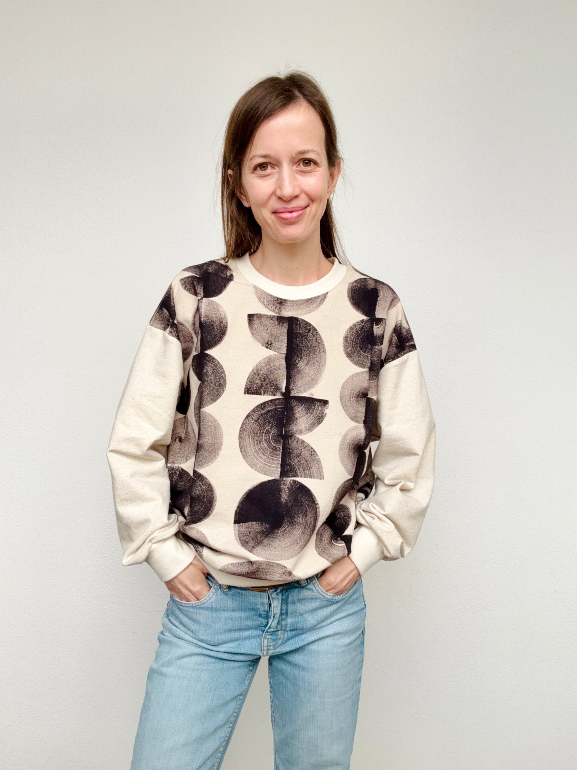 Woman wearing a natural black patterned sweater and jeans against a plain background