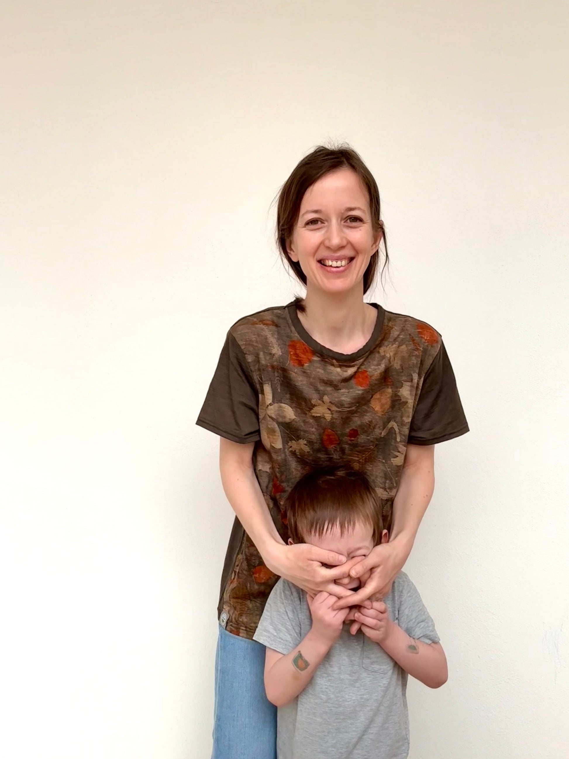 Woman and child wearing brown-gray naturally dyed t-shirt smiling against a white background