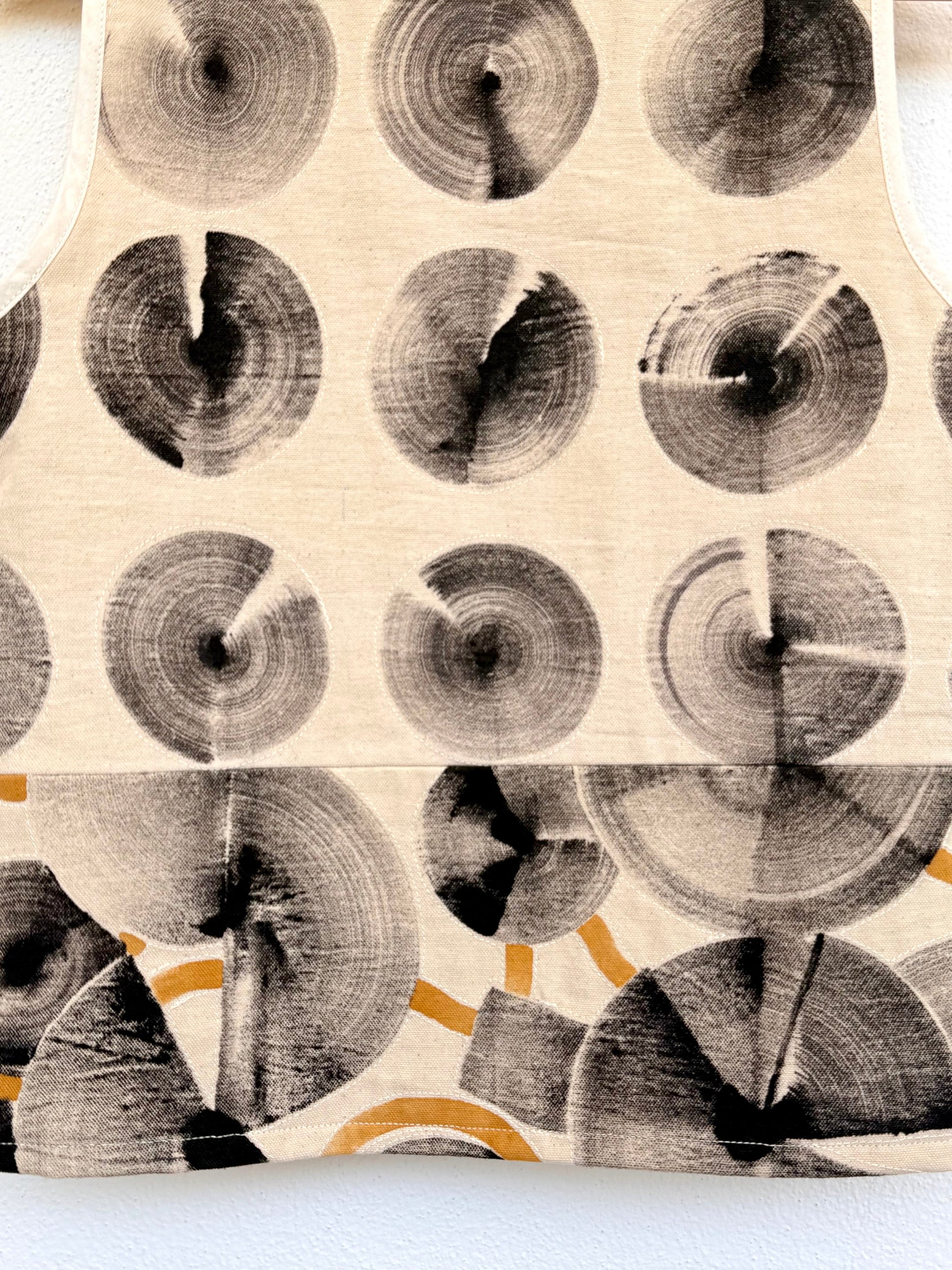 Tank top with circular hand-painted pattern on a wooden hanger against a white wall - close-up