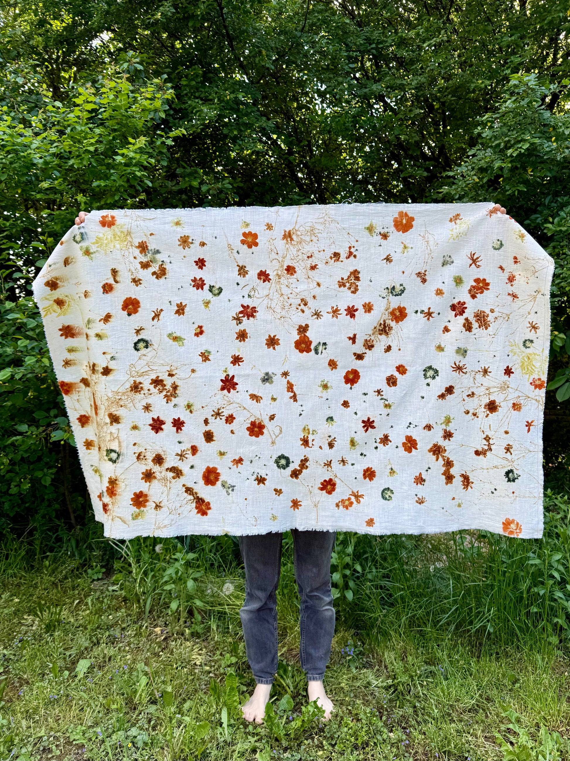 Person holding a large floral-patterned eco-printed fabric outdoors with greenery in the background