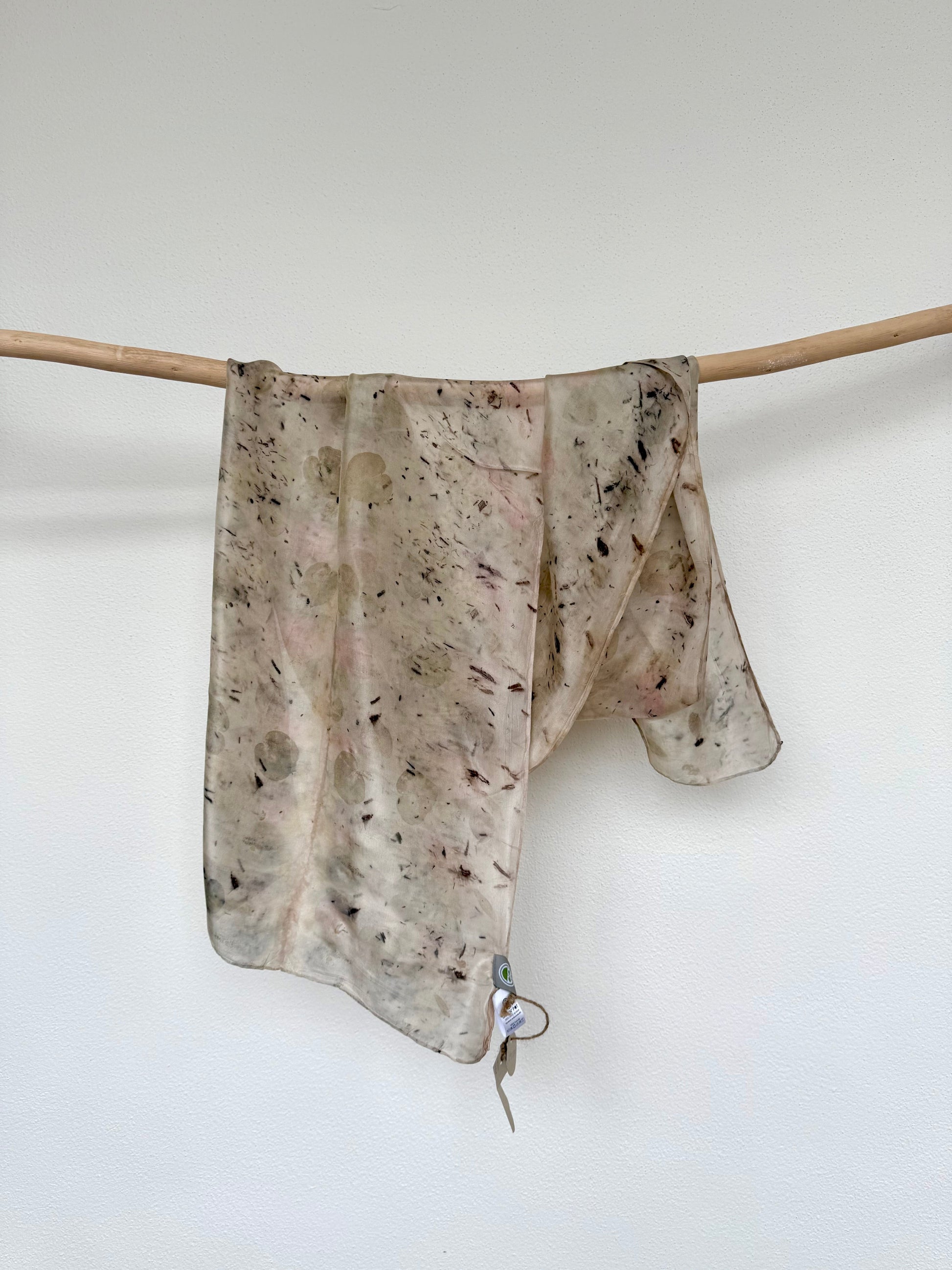 Light gray eco-printed and naturally dyed silk scarf with floral pattern on a wooden rod against a white background by DOT 'N' POT
