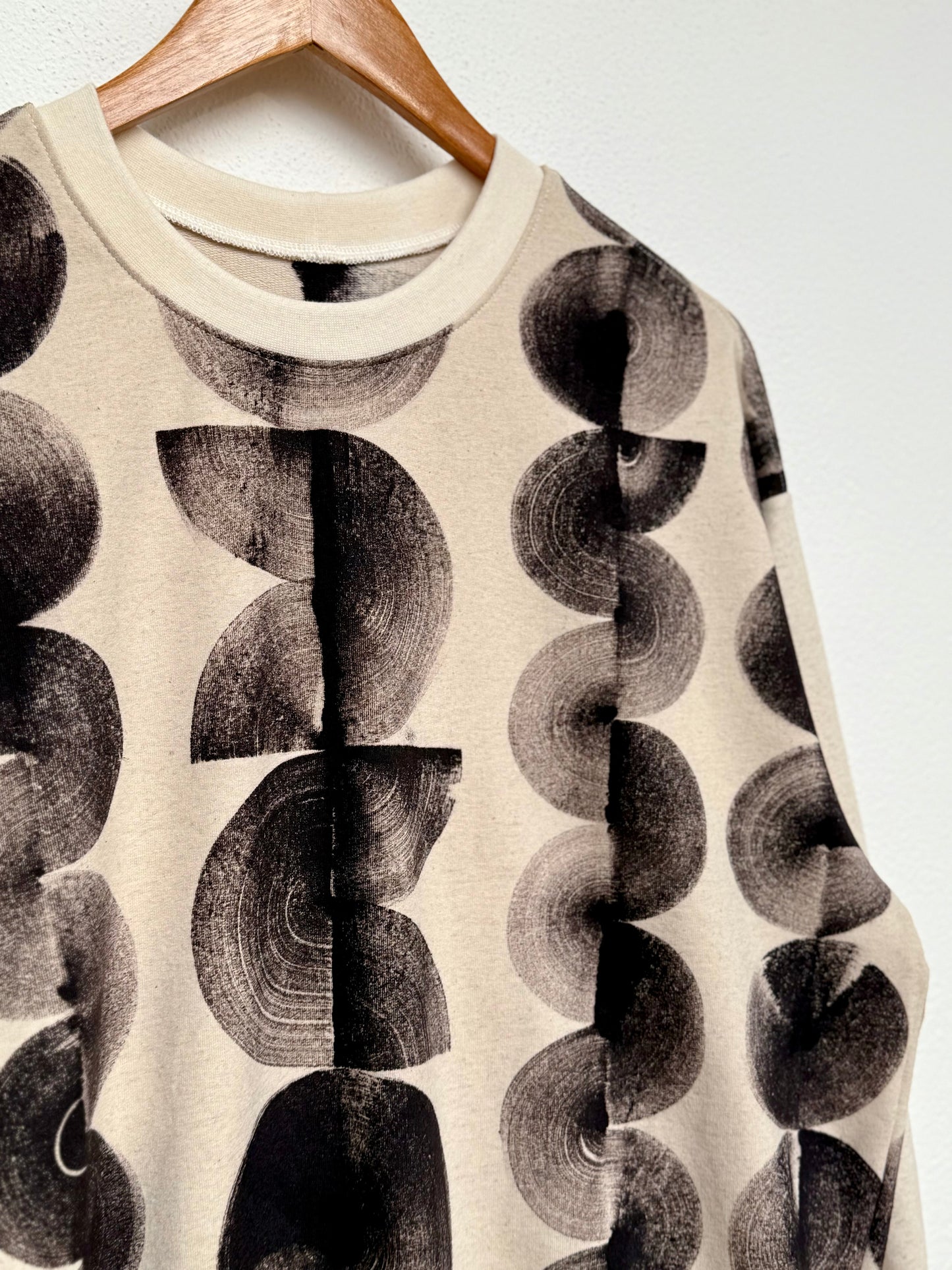 Beige sweater with black abstract pattern on a hanger against a white background