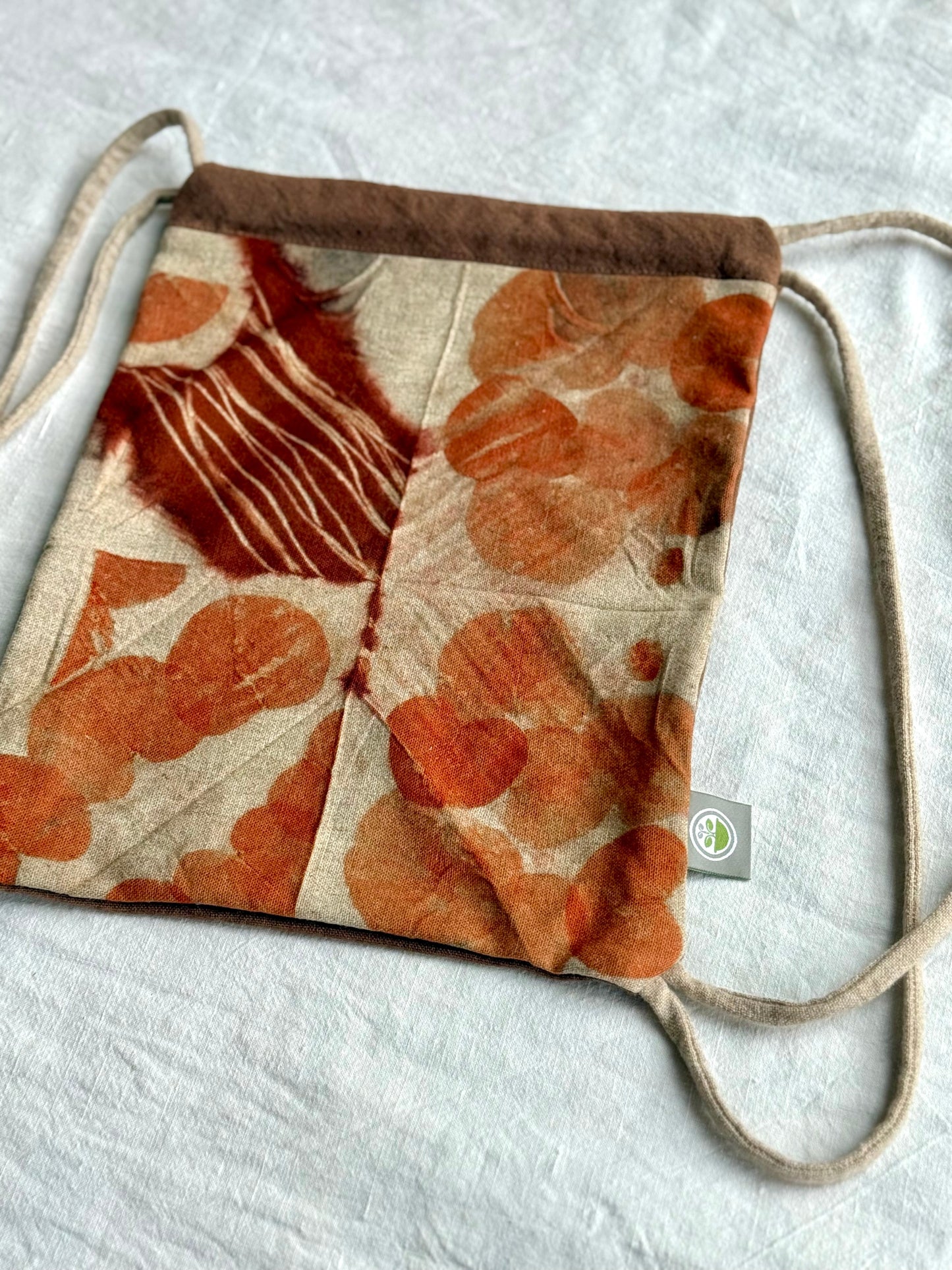 Drawstring bag naturally dyed and red-orange eco-printed on white background with DOT 'N' POT logo