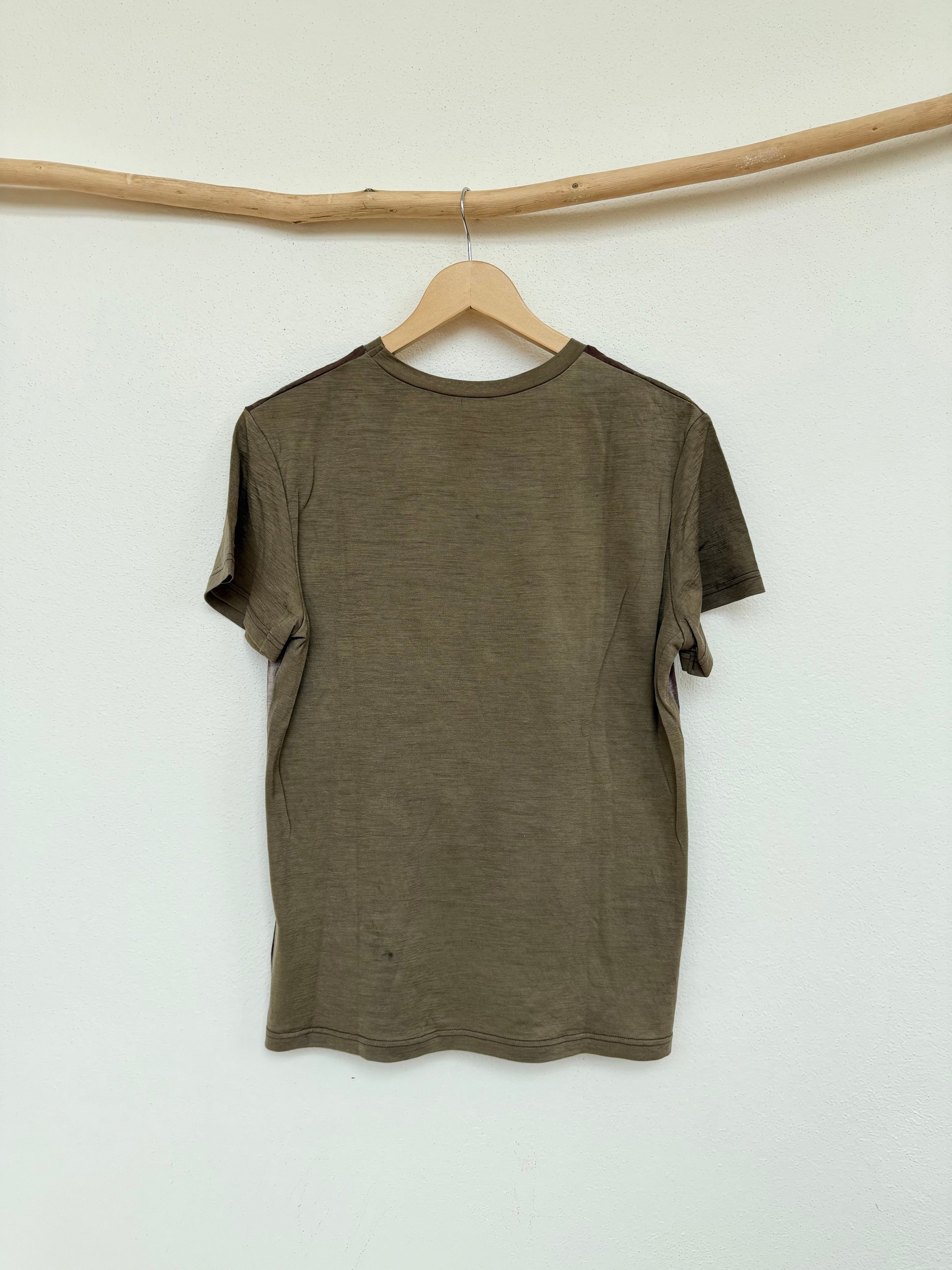 Green-gray naturally dyed t-shirt on a hanger against a white wall