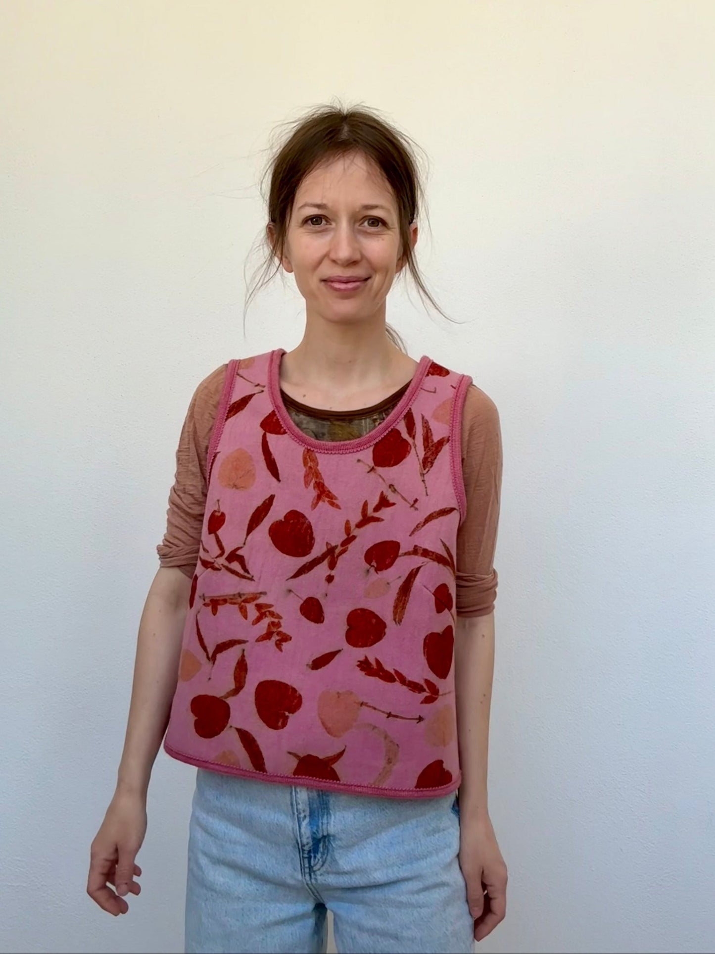 Woman wearing a pink vestwith red floral pattern against a white background