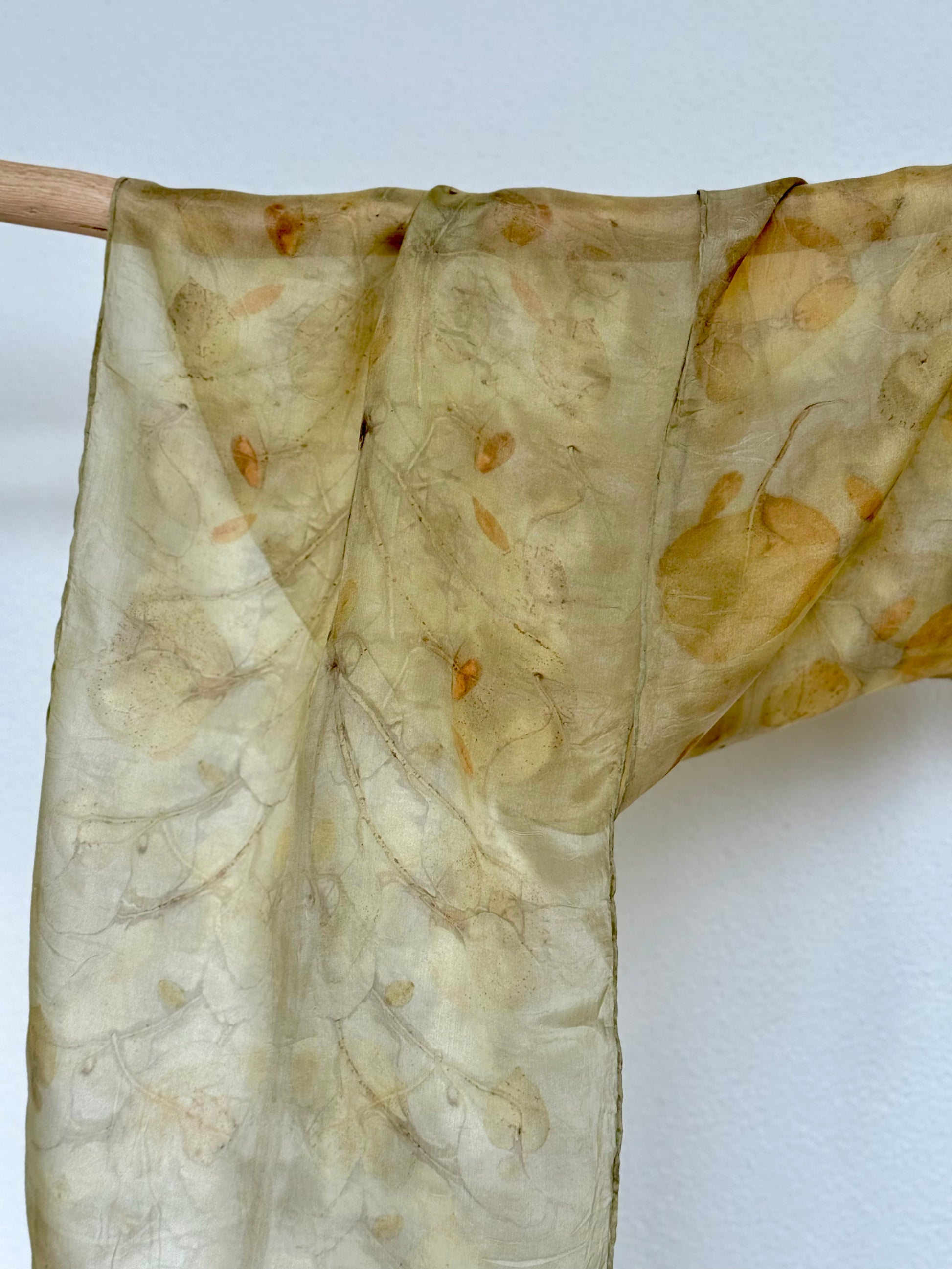 naturally dyed and eco-printed silk scarf hanging from a wooden rod against a white wall