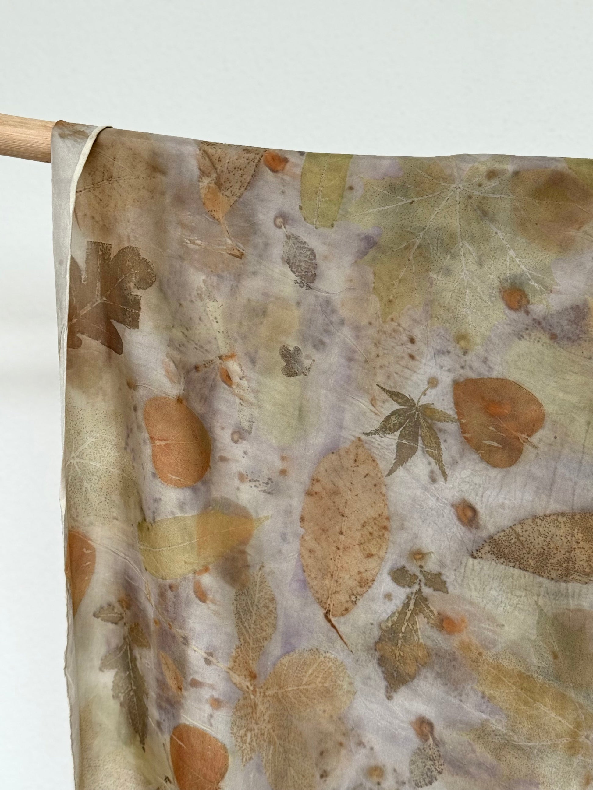 detail of an eco-printed silk scarf with floral pattern hanging on a wooden rod 