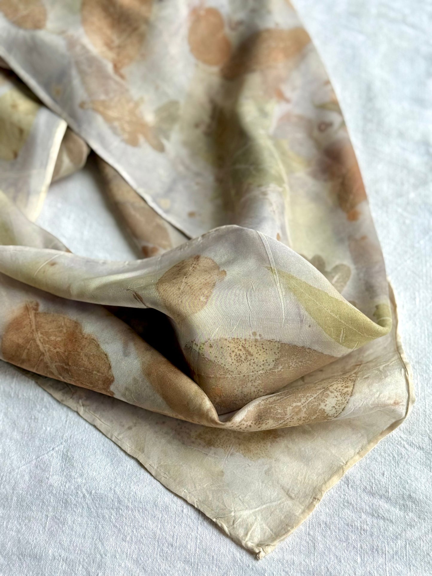 Folded silk scarf with brown and purple tones on a white background with floral logwood pattern