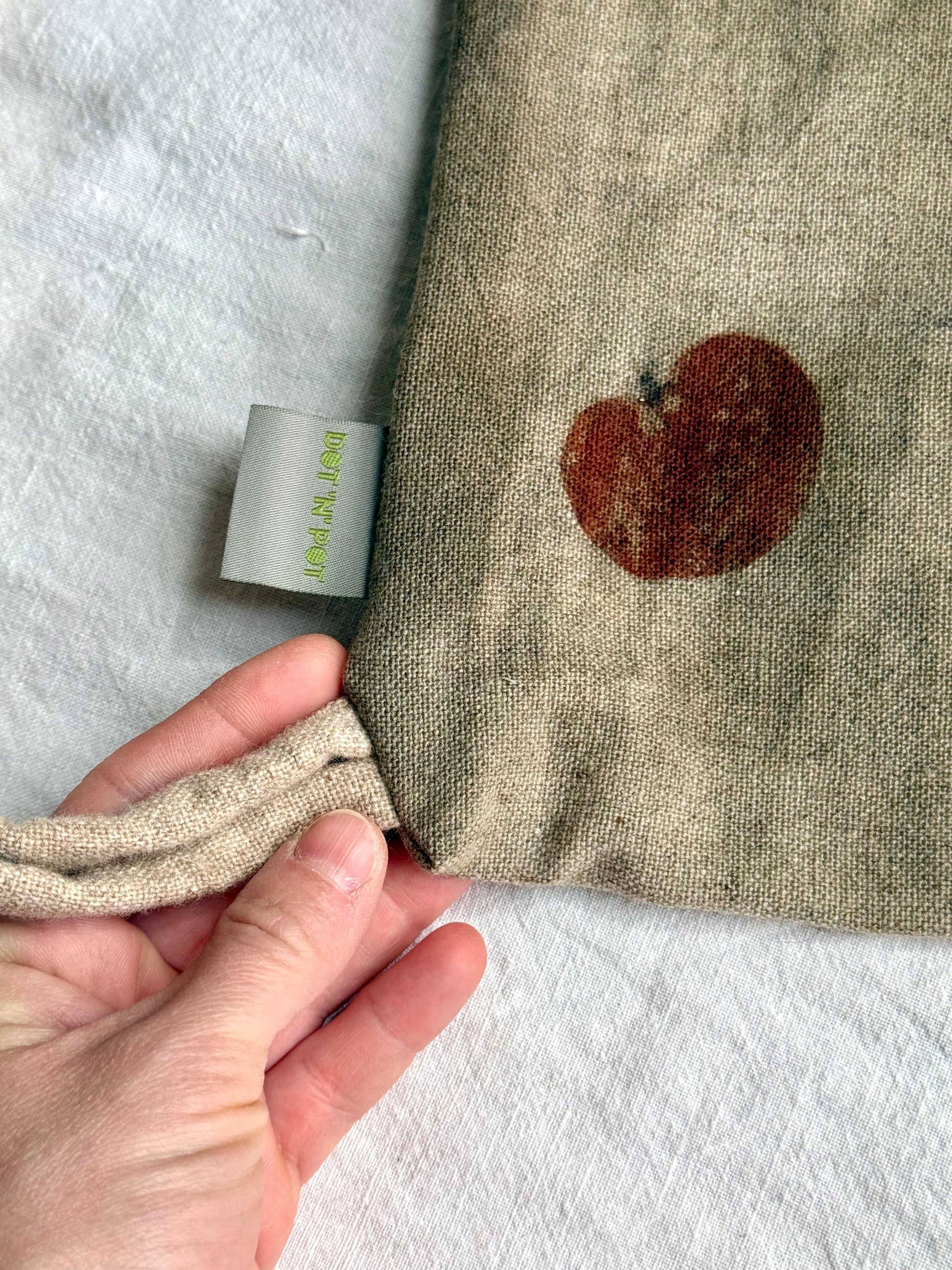 Woolen fabric bag with a heart shaped eucalyptus leaf design and a hand holding it, on a white background.