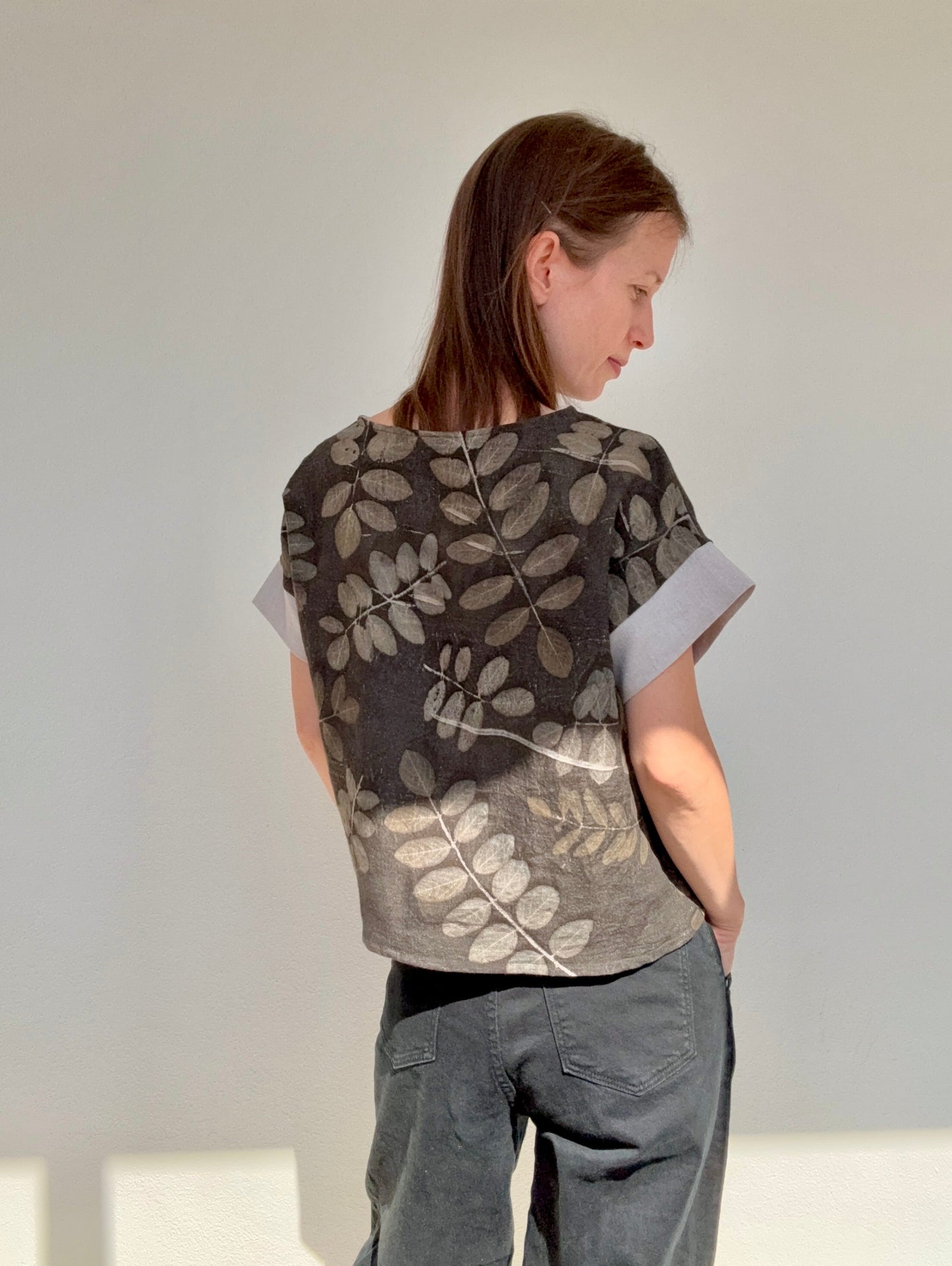 woman wearing and eco-printed and naturally gray dyed robinia leaves patterned linen top against a white background