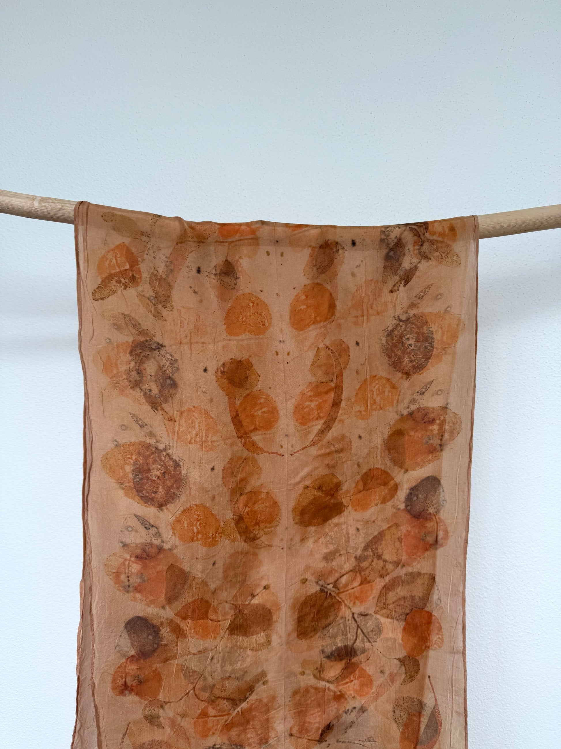 Silk scarf with leaf pattern hanging on a rod against a light background