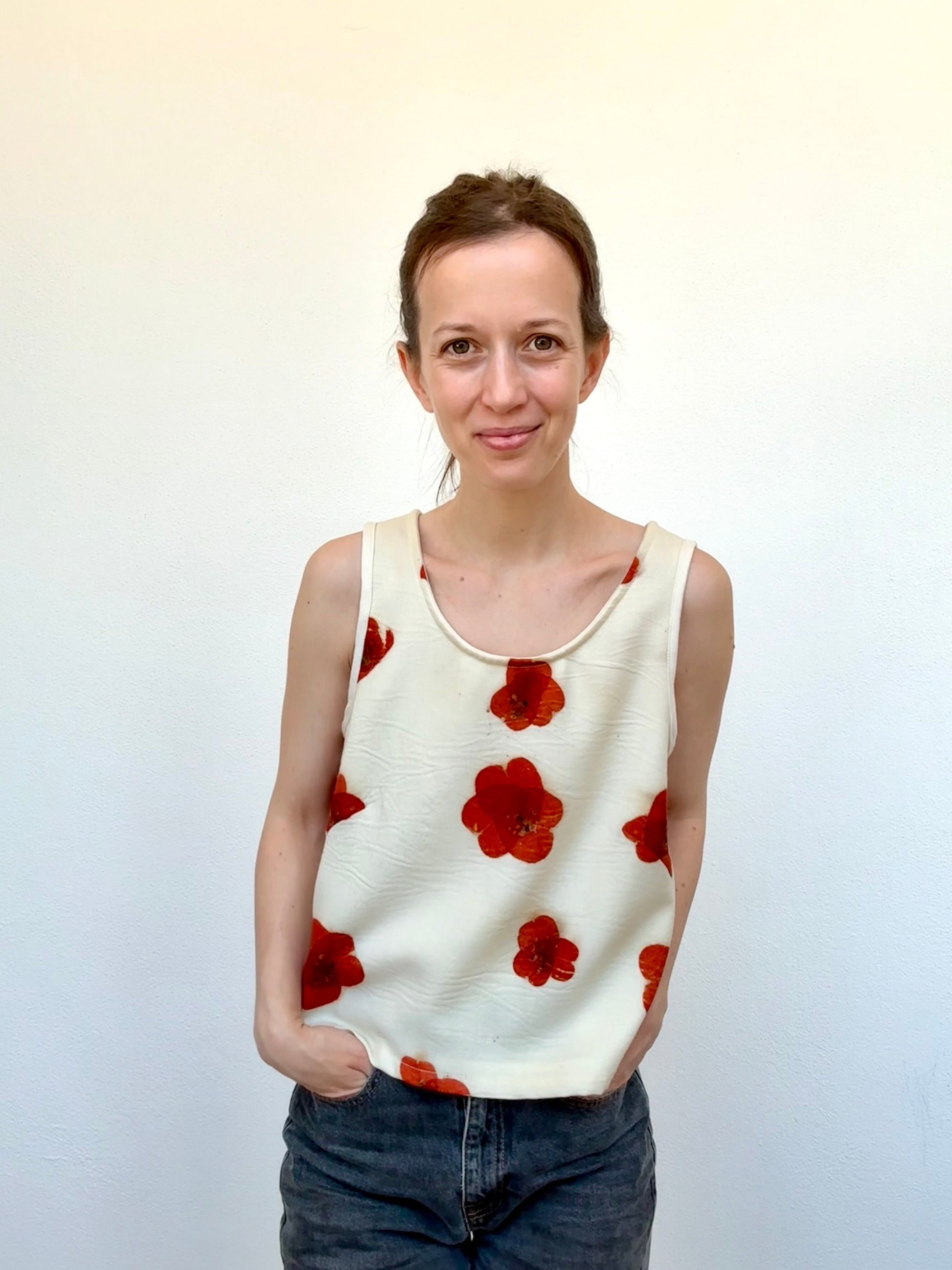 Woman wearing a sleeveless merino wool top with red floral poppy pattern against a plain background