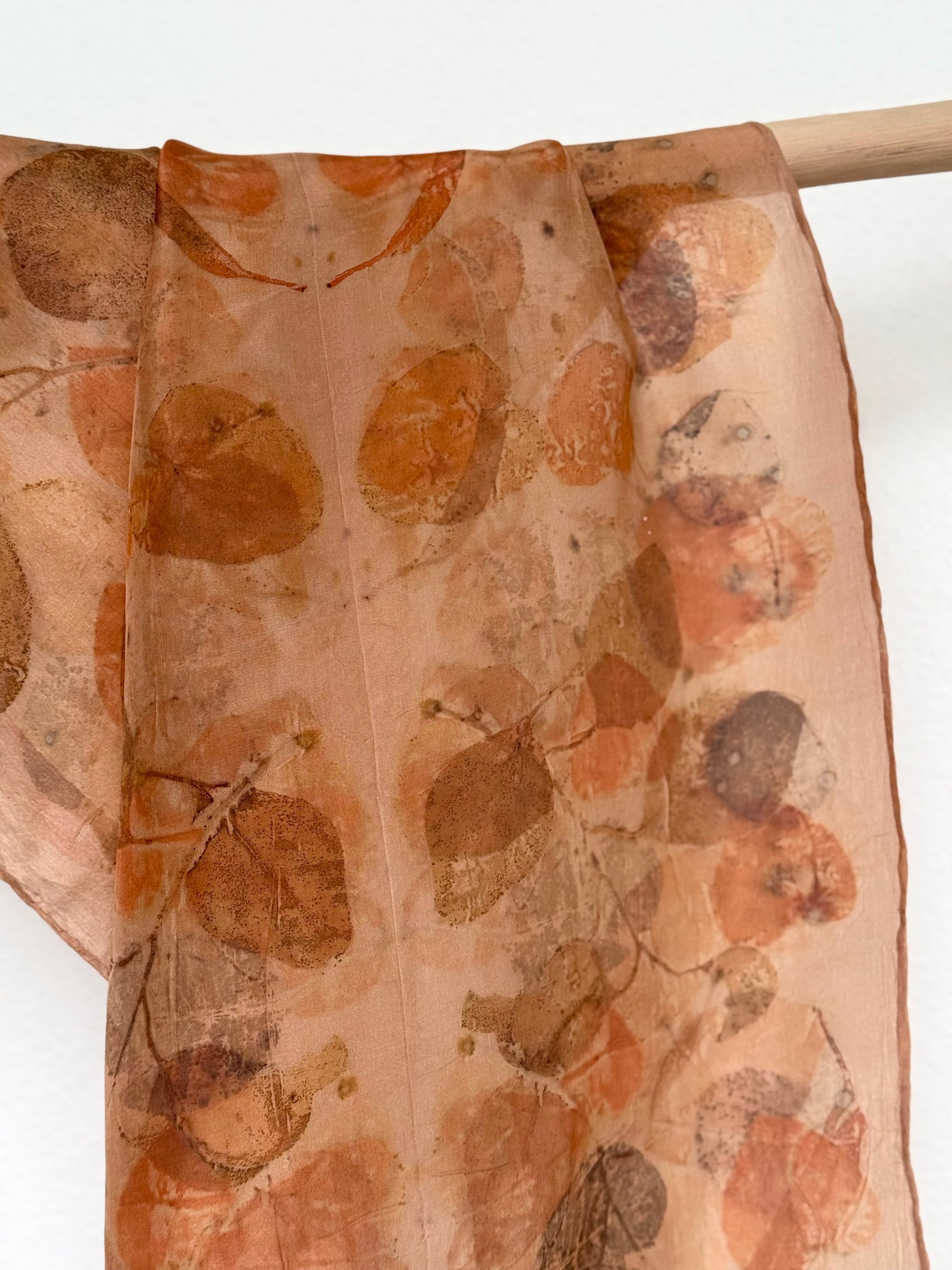 close-up of a naturally dyed eucalyptus silk scarf hanging from a wooden rod 