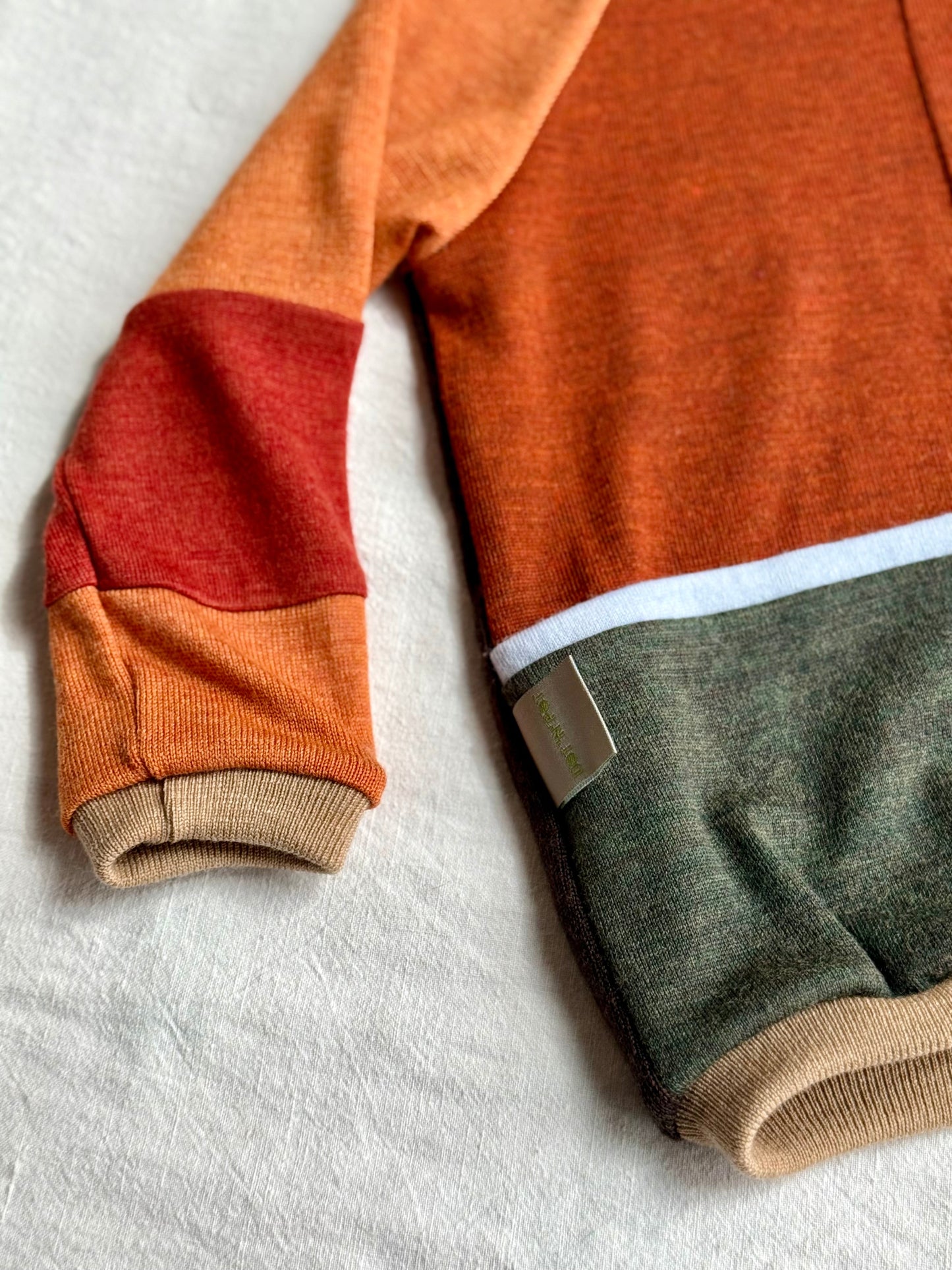 Detail of a colorful merino wool sweater upcycled from orange, red, light blue and green colours 