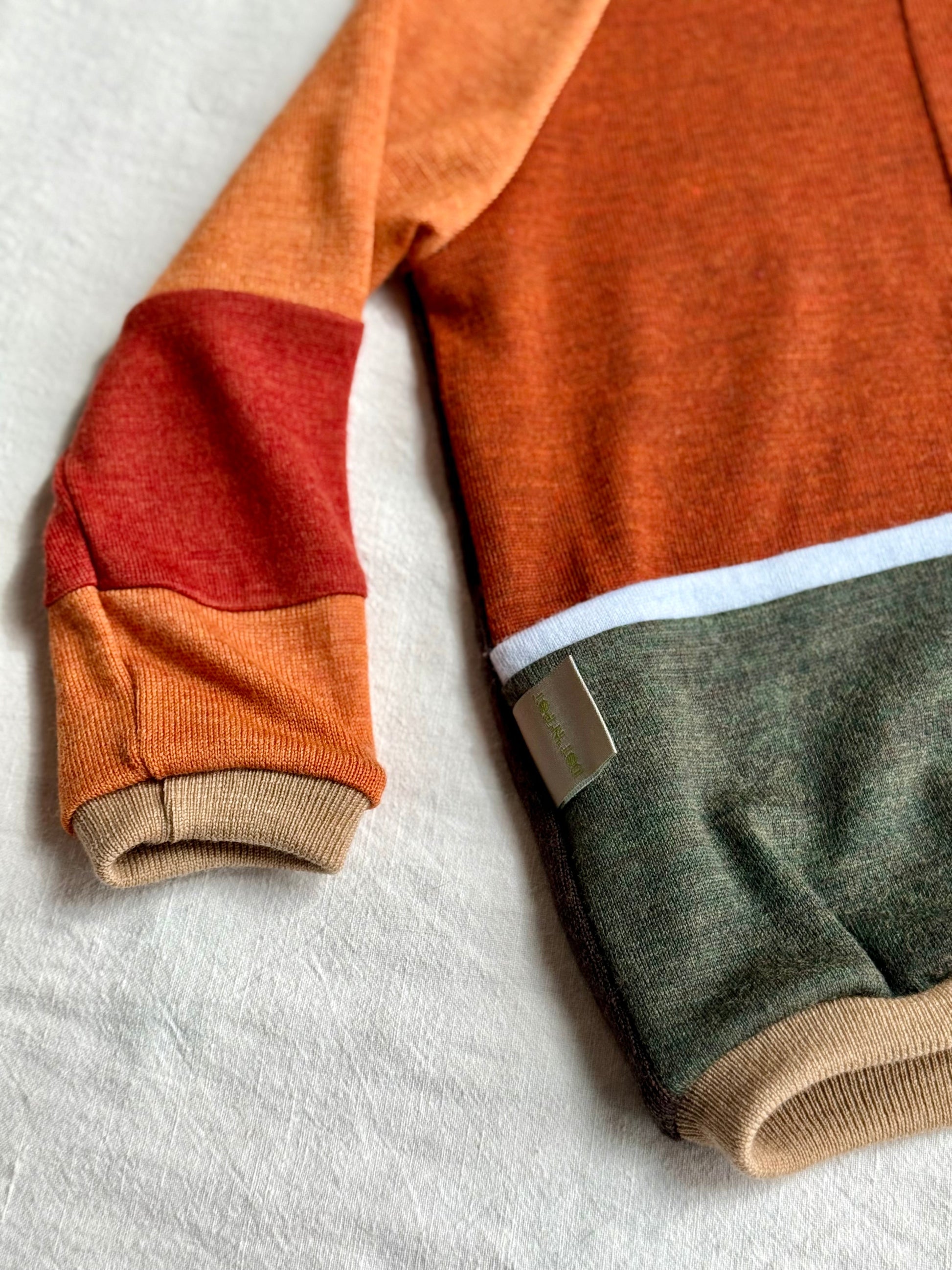 Detail of a colorful merino wool sweater upcycled from orange, red, light blue and green colours 