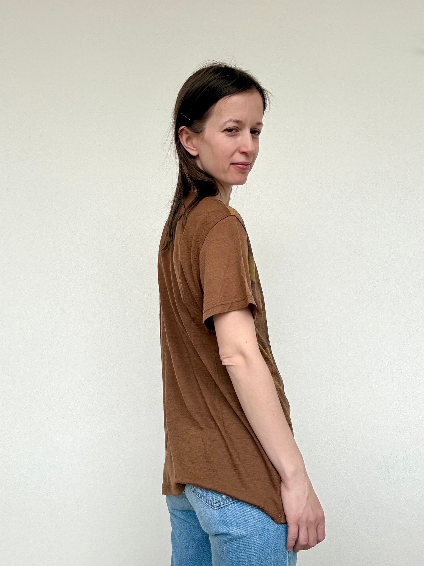 Woman wearing a naturally dyed brown walnut husks t-shirt and blue jeans against a white background