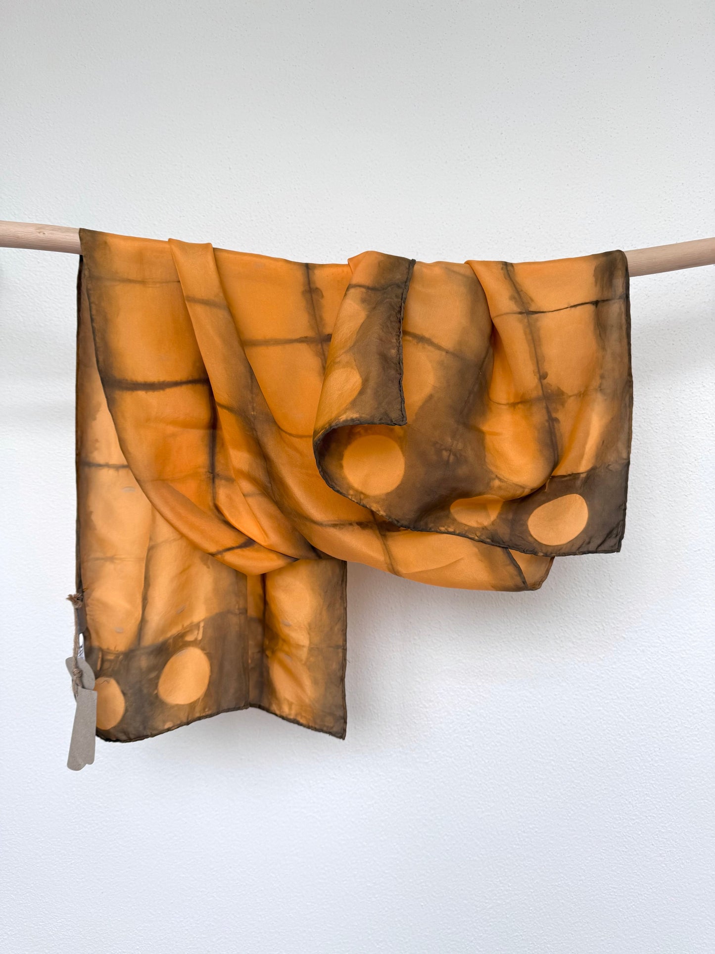 Brown and orange patterned silk scarf draped over a rod against a white background by DOT 'N' POT