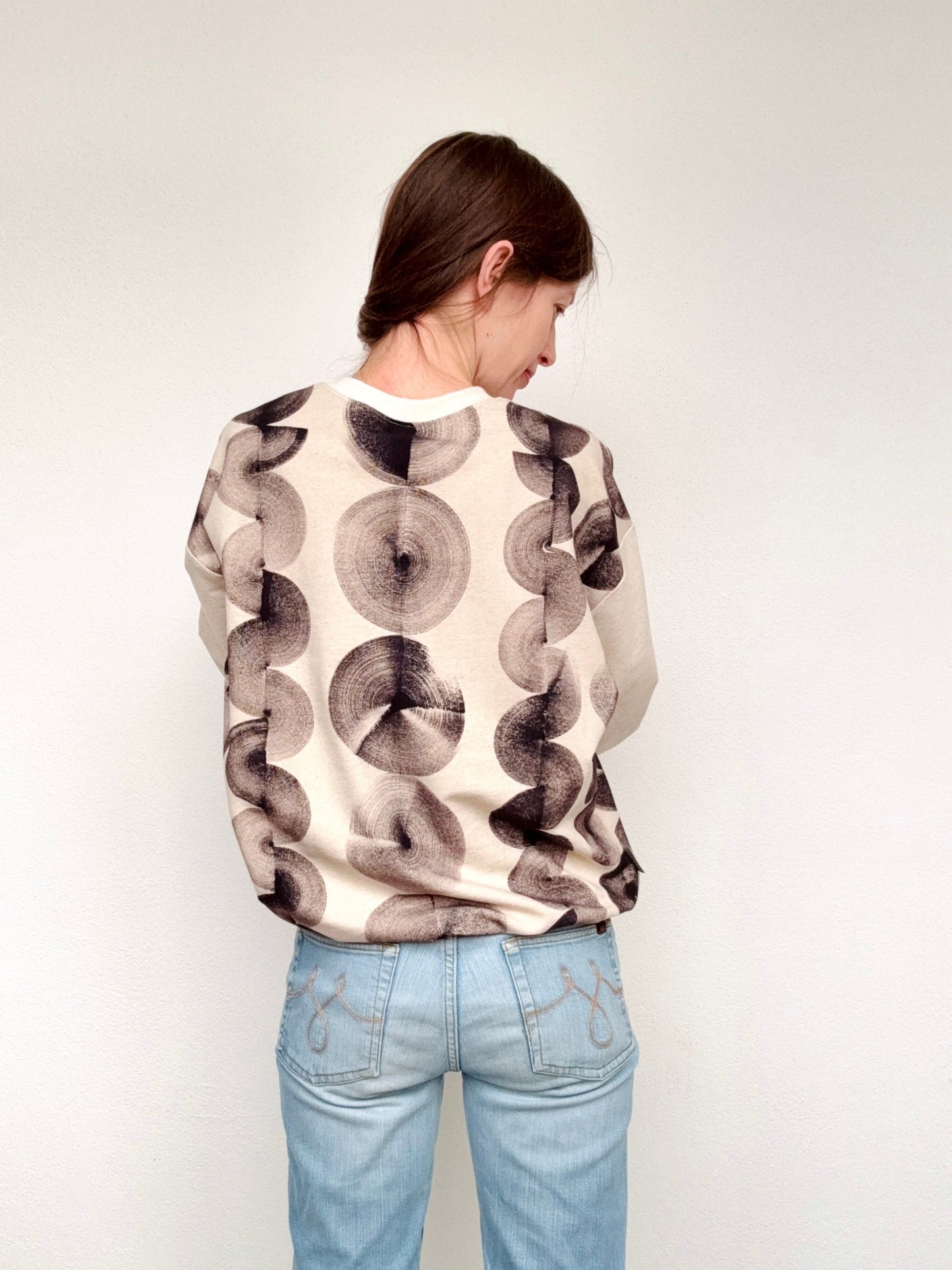 Person wearing a hand-painted, black patterned sweater and light blue jeans against a plain background by DOT 'N' POT