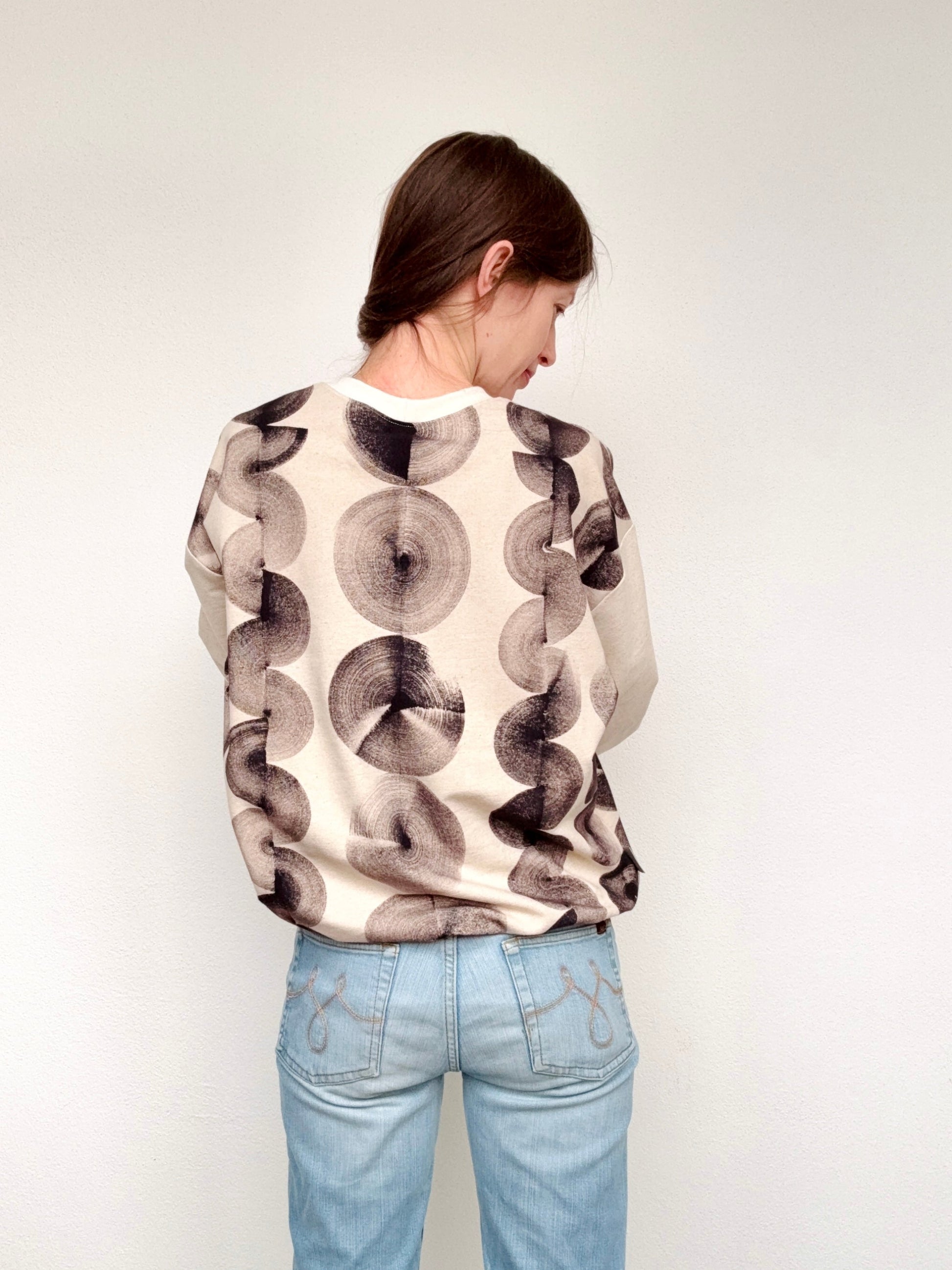 Person wearing a hand-painted, black patterned sweater and light blue jeans against a plain background by DOT 'N' POT