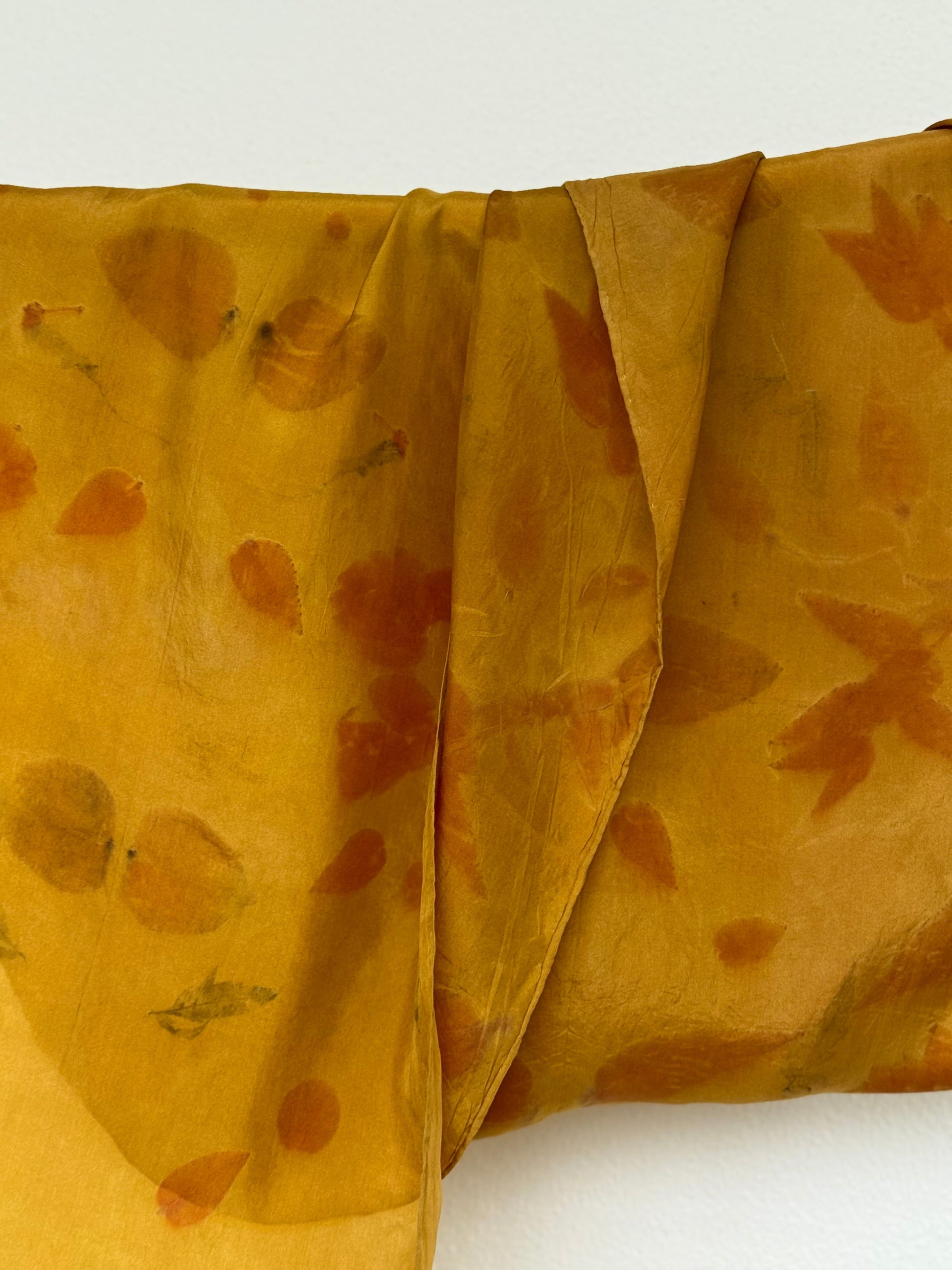 silk scarf naturally dyed with onion skins and eco-printed with eucalyptus leaves hanging against white background
