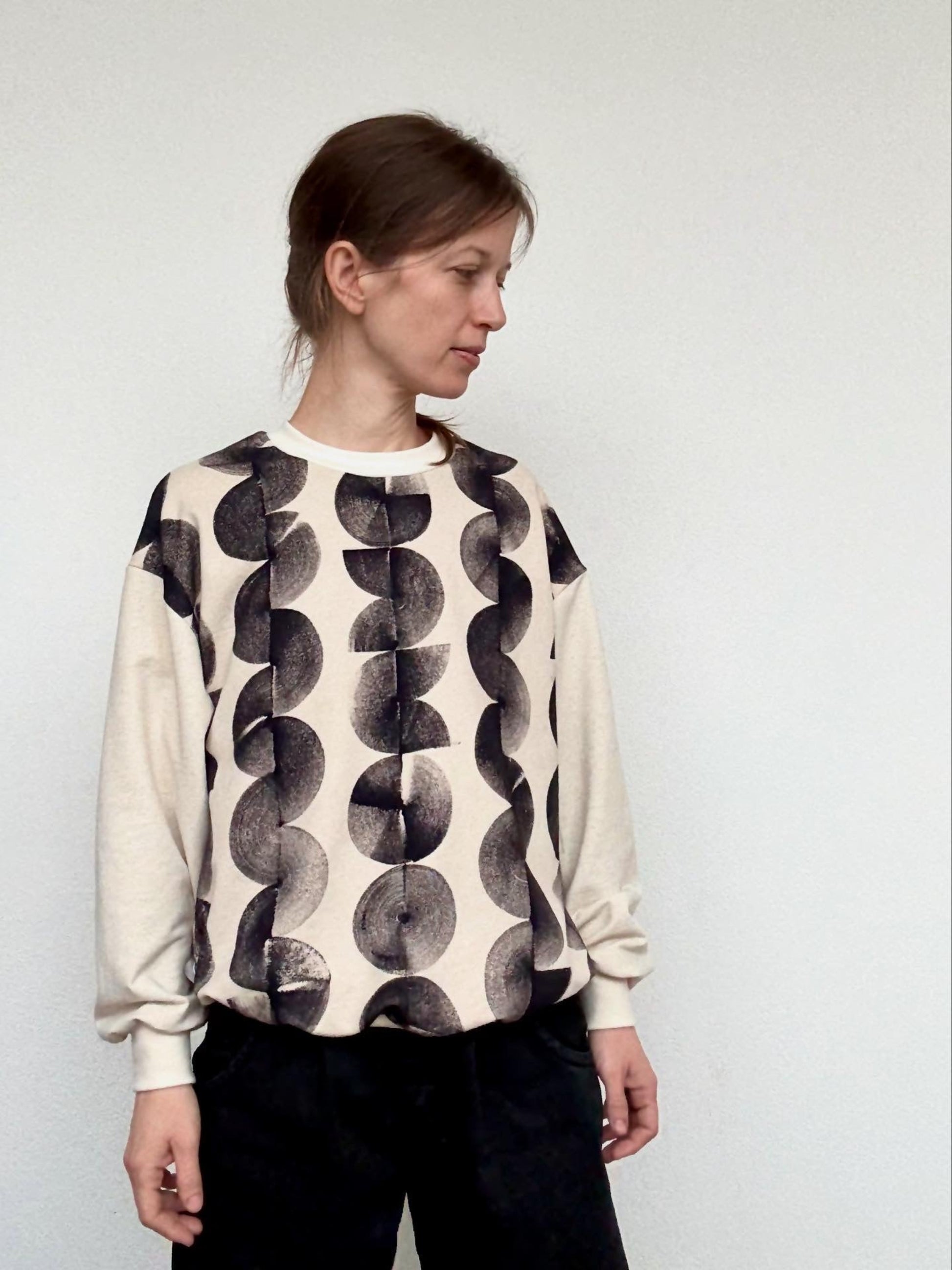 Woman wearing a natural cream colored linen sweater with black abstract, hand-painted pattern against a plain background