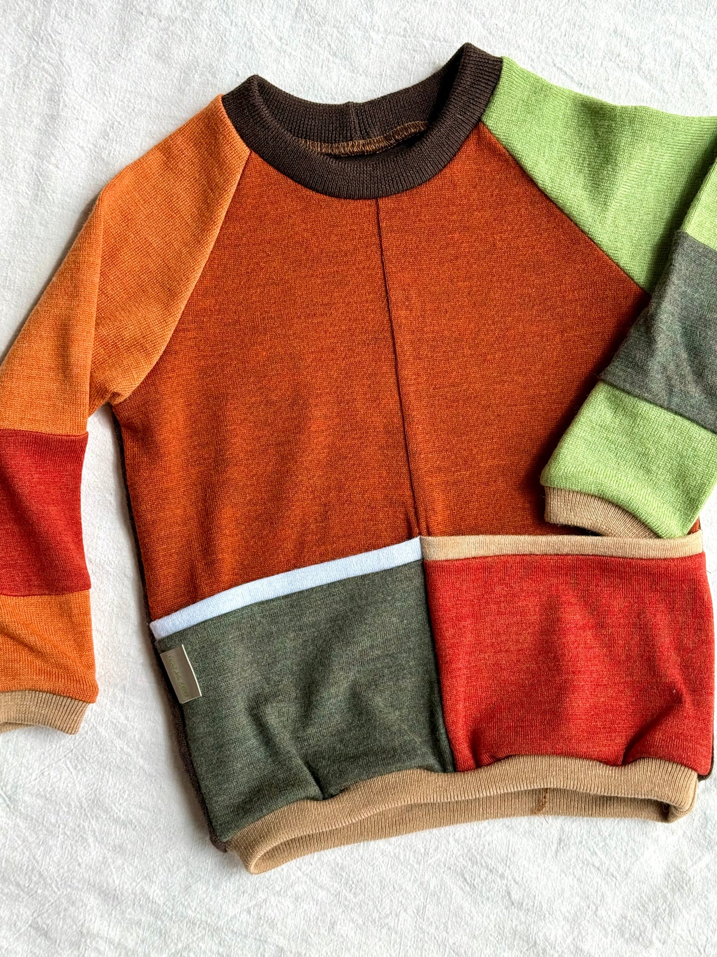 upcycled merino swetaer with orangesm brown, red and green colours on white background