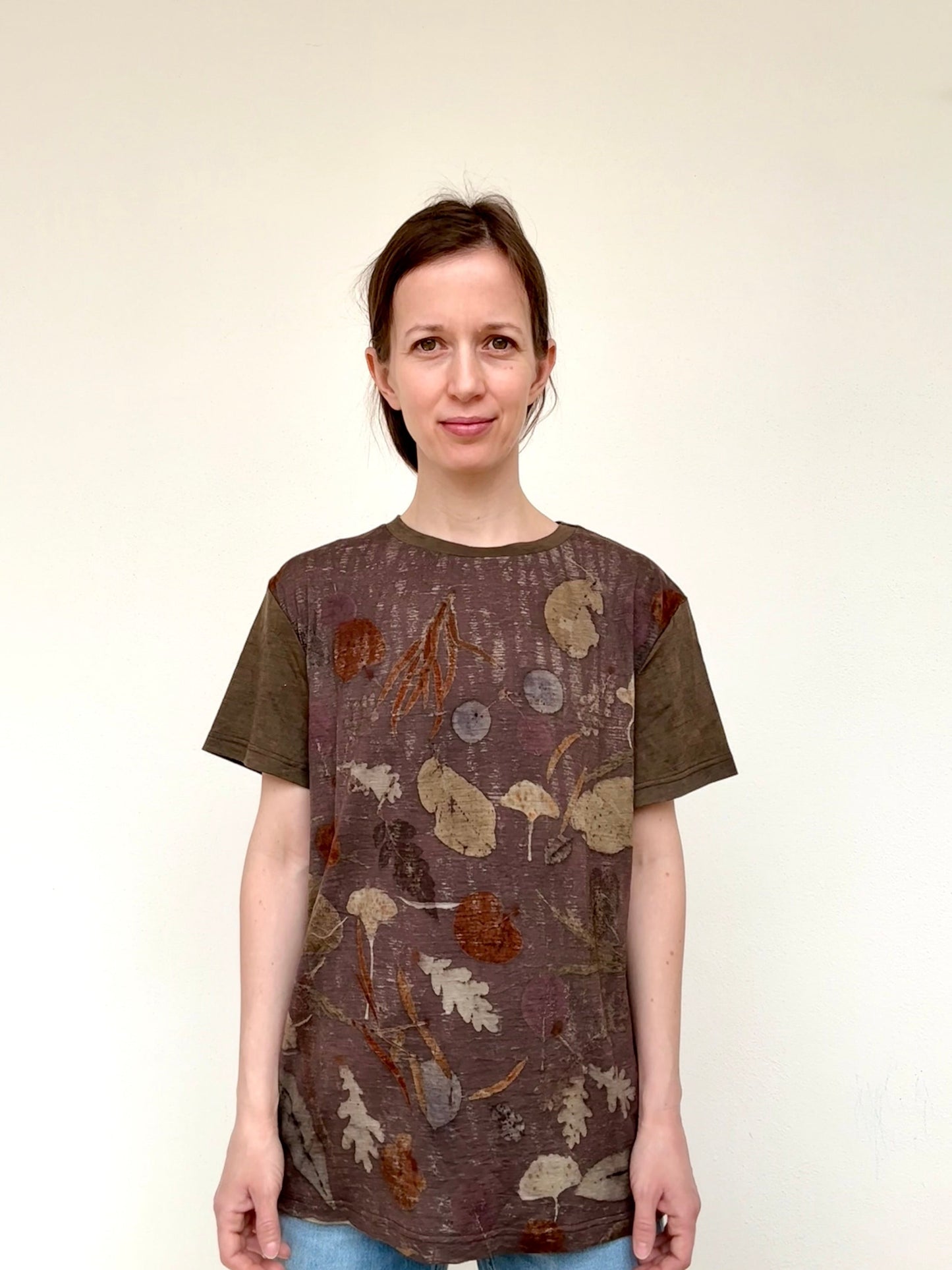 Woman wearing a brown-purple swett chestnut dyed and ec-printed t-shirt with leaves against a white background