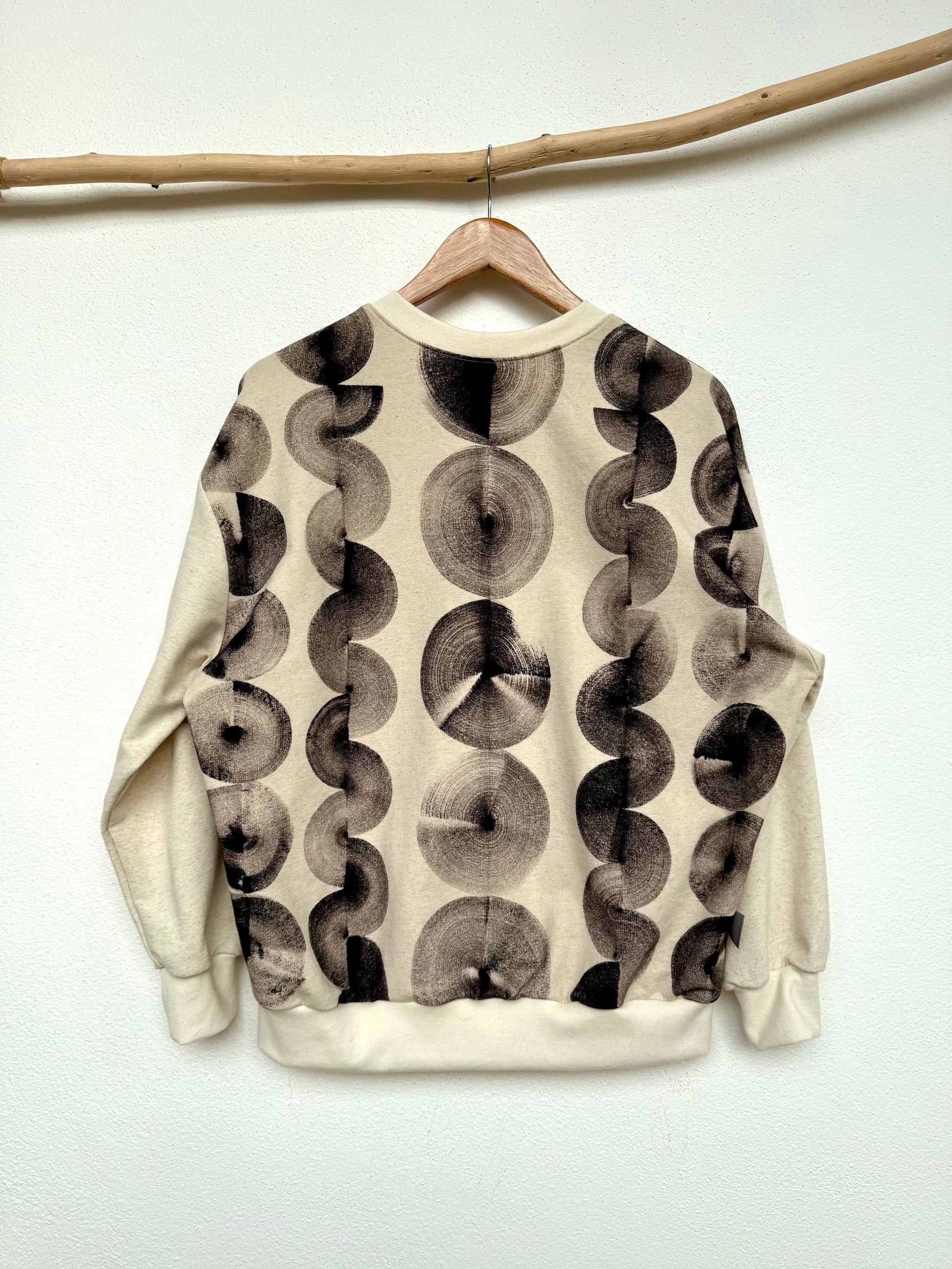 Sweatshirt with natural black abstract hand-painted pattern hanging on a wooden rod against a white wall by DOT 'N' POT