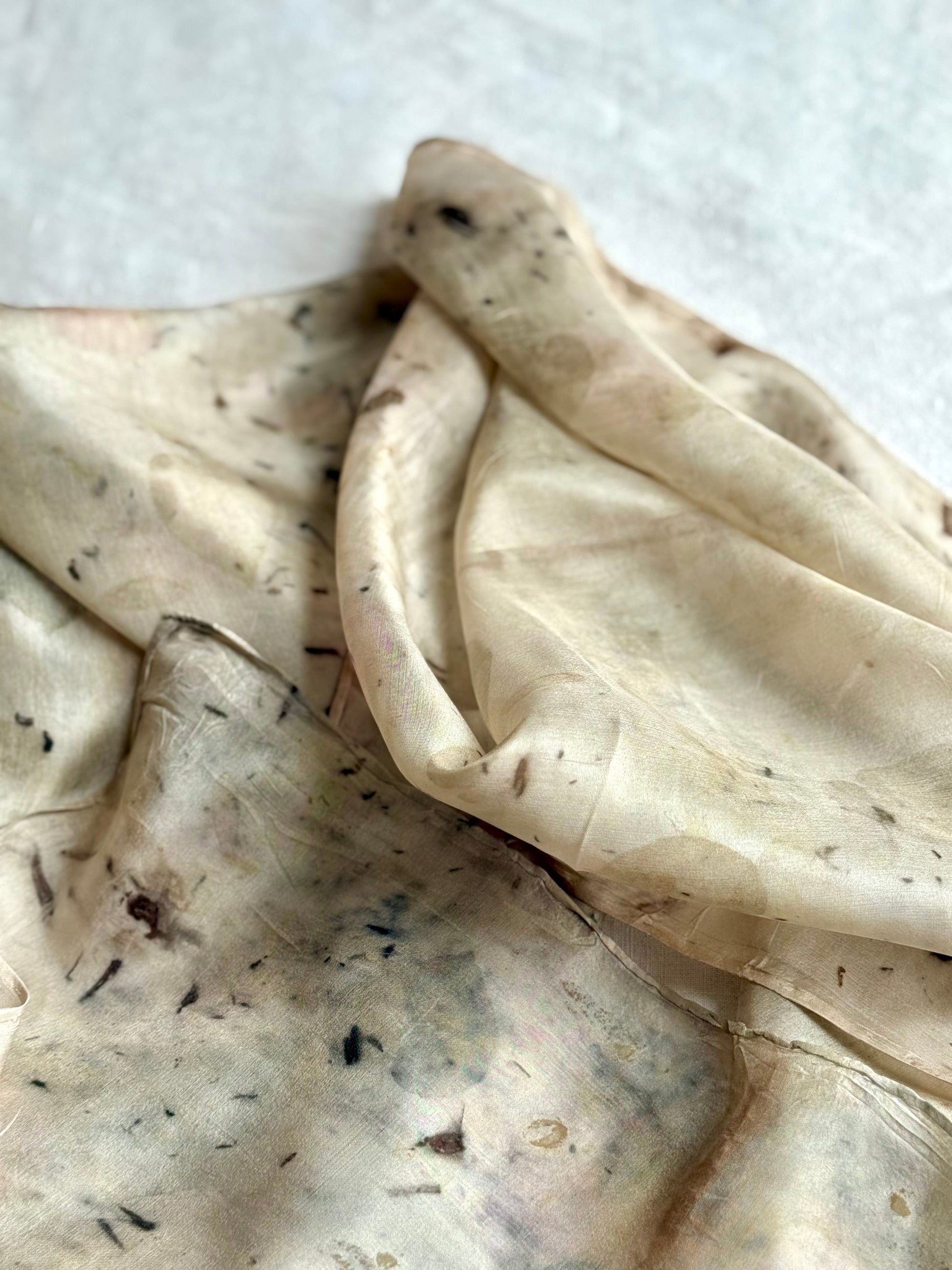 Close-up of a textured gray silk scarf with dark specks on a white background