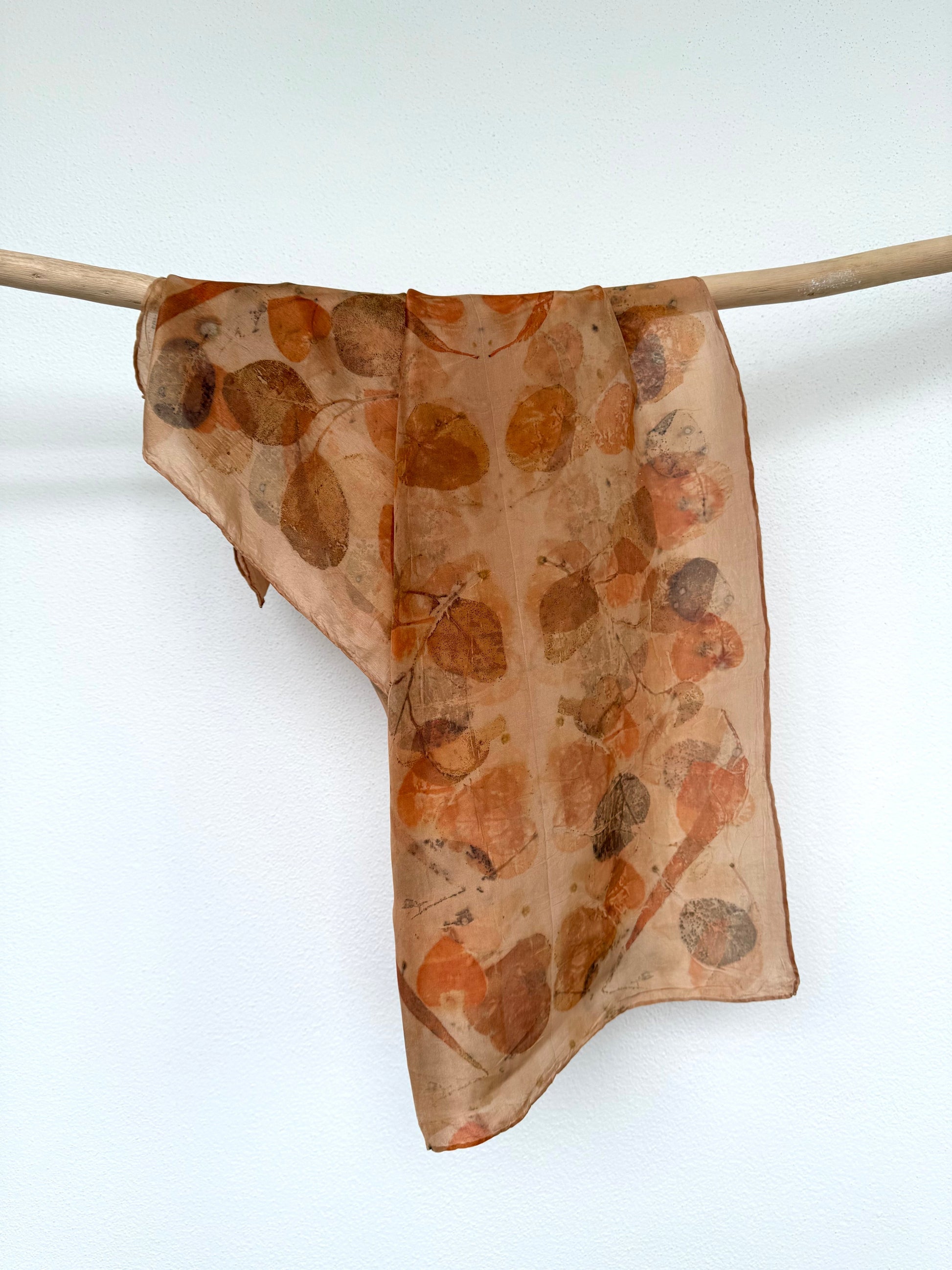 naturally dyed and ecoprinted silk scarf hanging from a wooden rod by DOT 'N' POT
