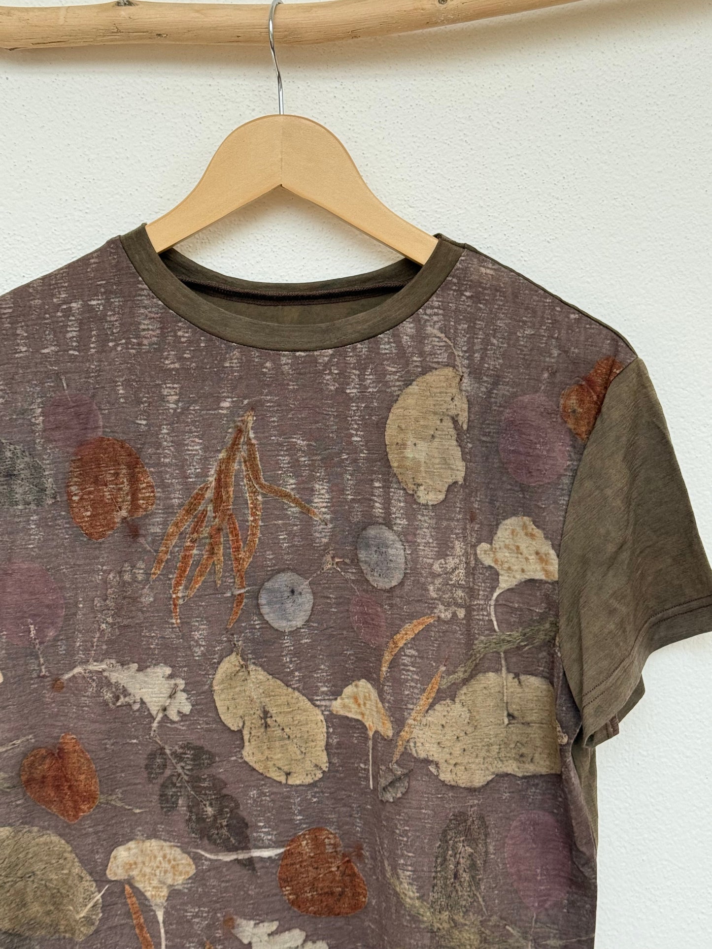 T-shirt with natural eco-print pattern on a wooden hanger against a white wall - close-up of the front part with neckline