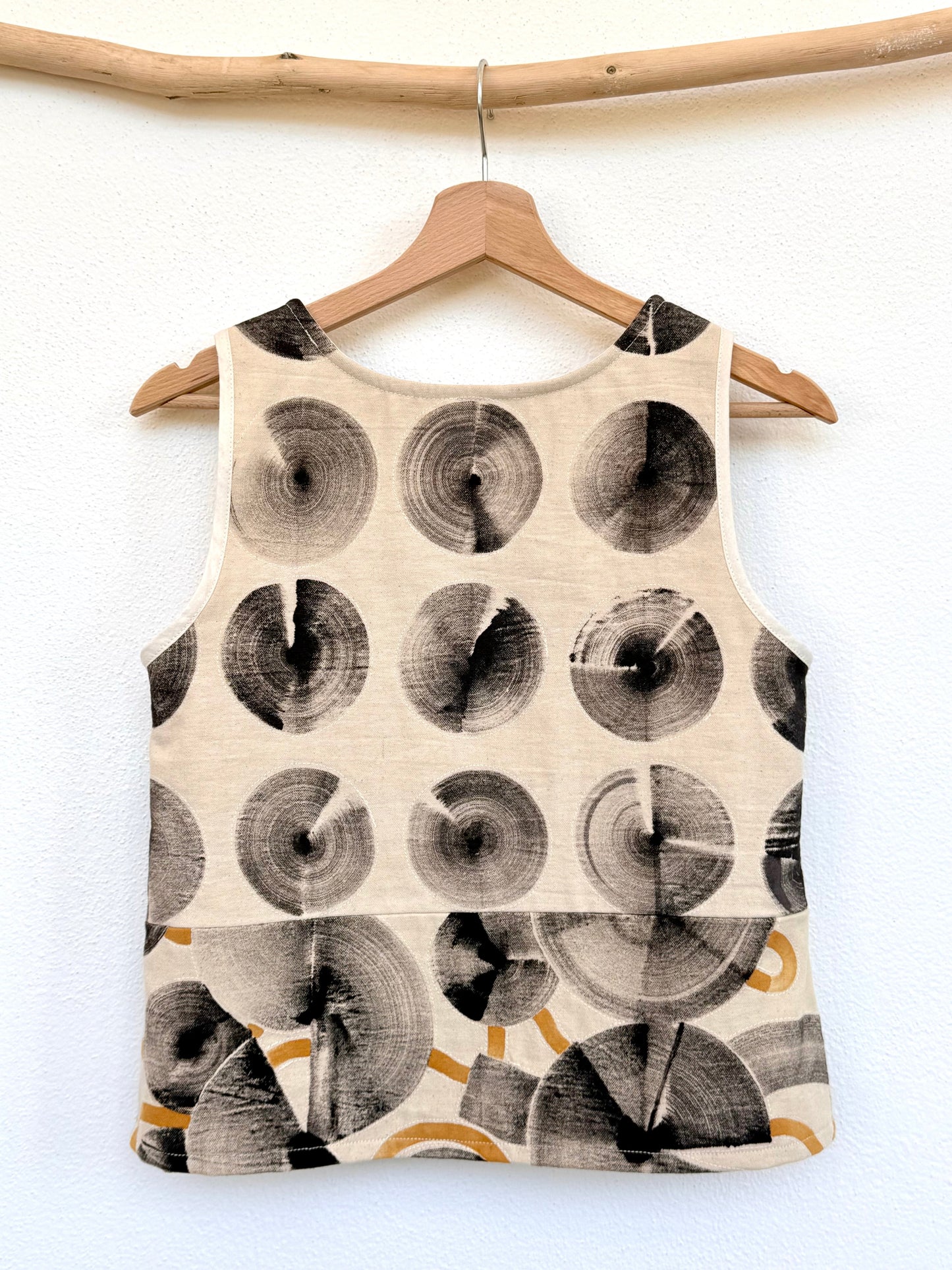 Tank top with a naturally colored circular hand-painted pattern on a wooden hanger against a white wall by DOT 'N' POT