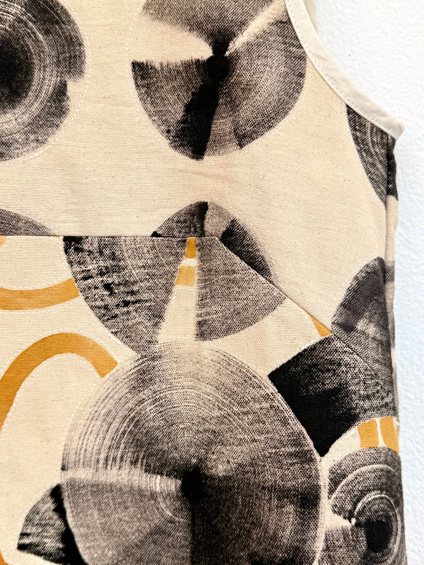 Close-up of a textured fabric with naturally dyed abstract patterns in black, gray, and orange on a beige background.
