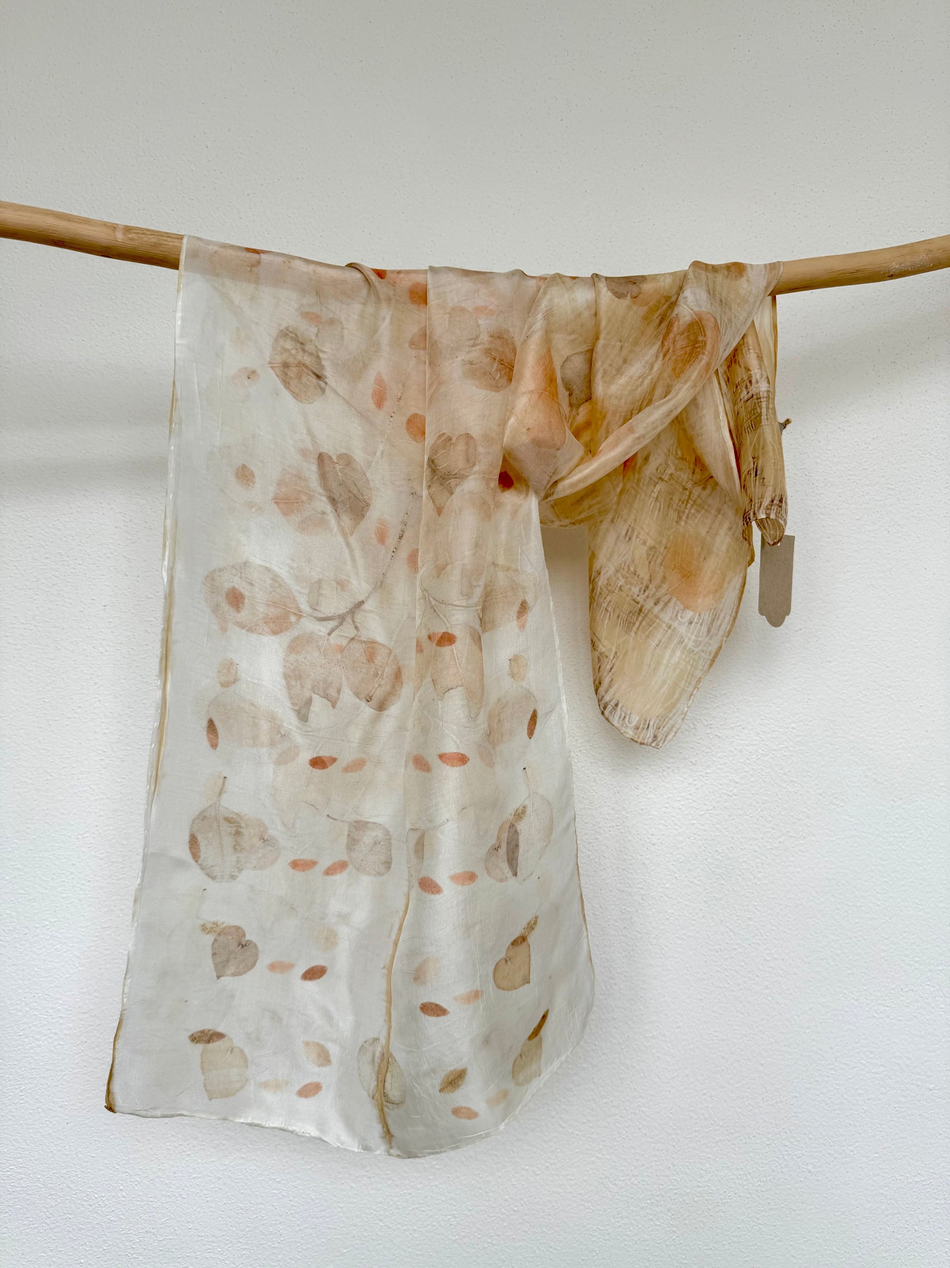 silk scarf with natural eco-print made with eucalyptus leaves by DOT 'N' POT hanging on a wooden rod against white background