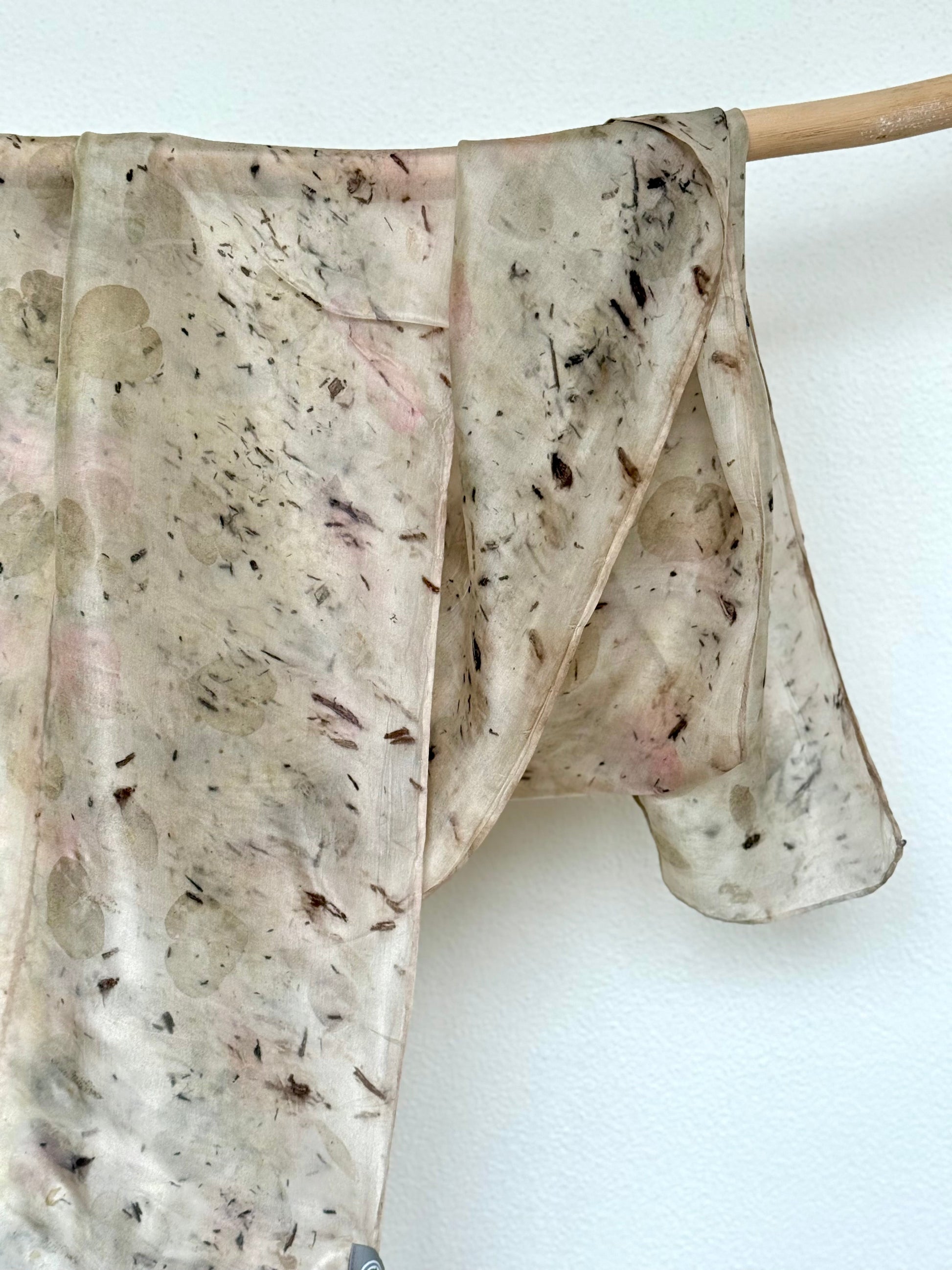 Textured silk scarf with dark logwood specks on a white background hanging from a wooden rod by DOT 'N' POT