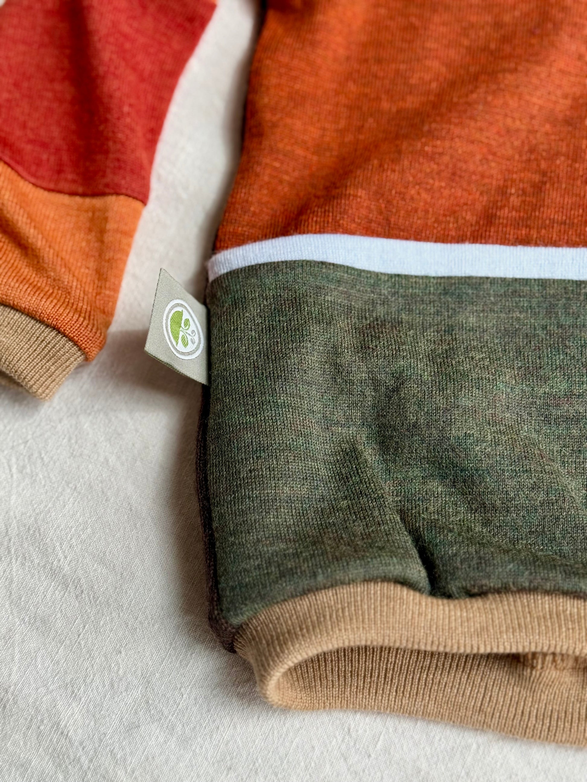 Close-up of a merino wool sweater with color-blocked design and a visible tag with logo by DOT 'N' POT
