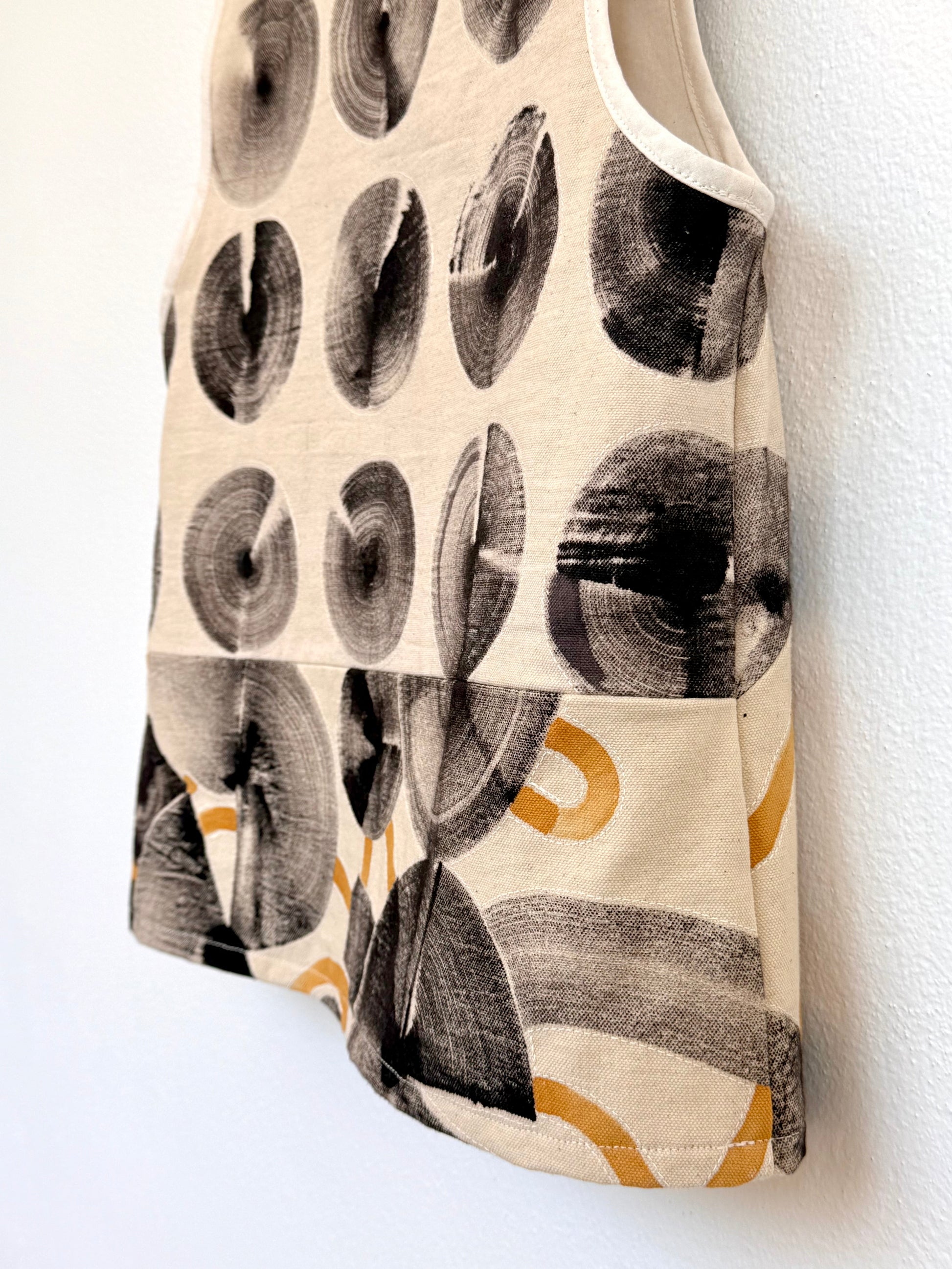 Tank top with natural, ferrous paste circular hand-painted pattern on a wooden hanger against a white wall - close-up of the sewing